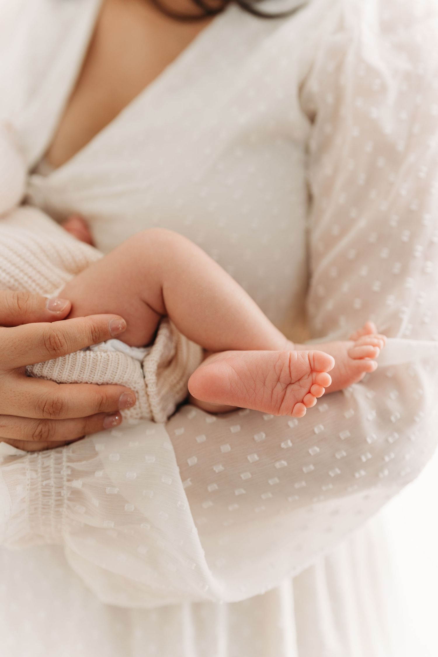 Petits pieds délicats de bébé dans les bras de sa maman qui le tient avec amour lors de la séance nouveau-né fine art à Québec