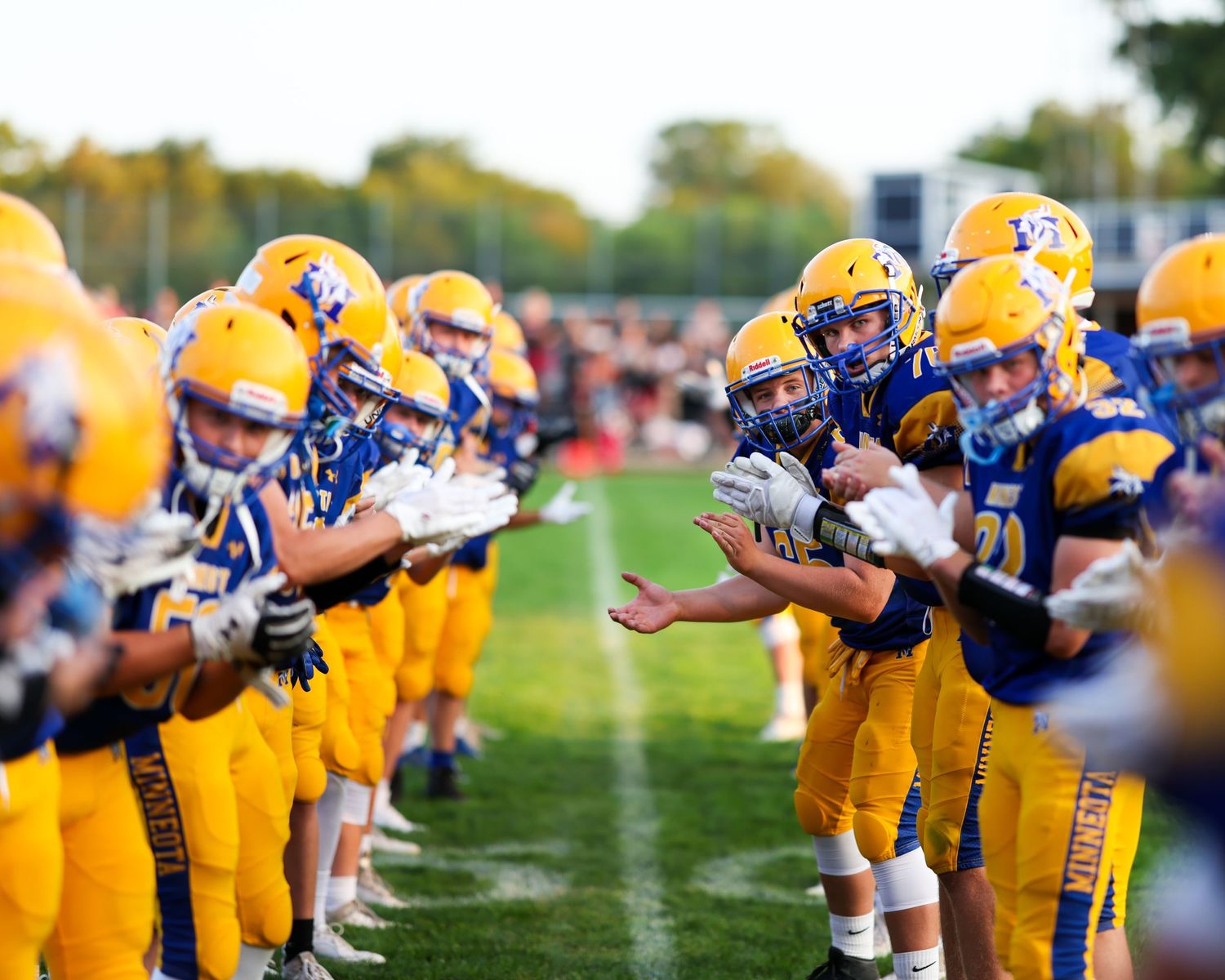 Youth football players in gold and blue uniforms face off in a high-energy pre-game lineup.