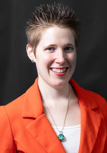 A sequence of four headshots showing someone in an orange blazer and white top against a dark background, smiling progressively.