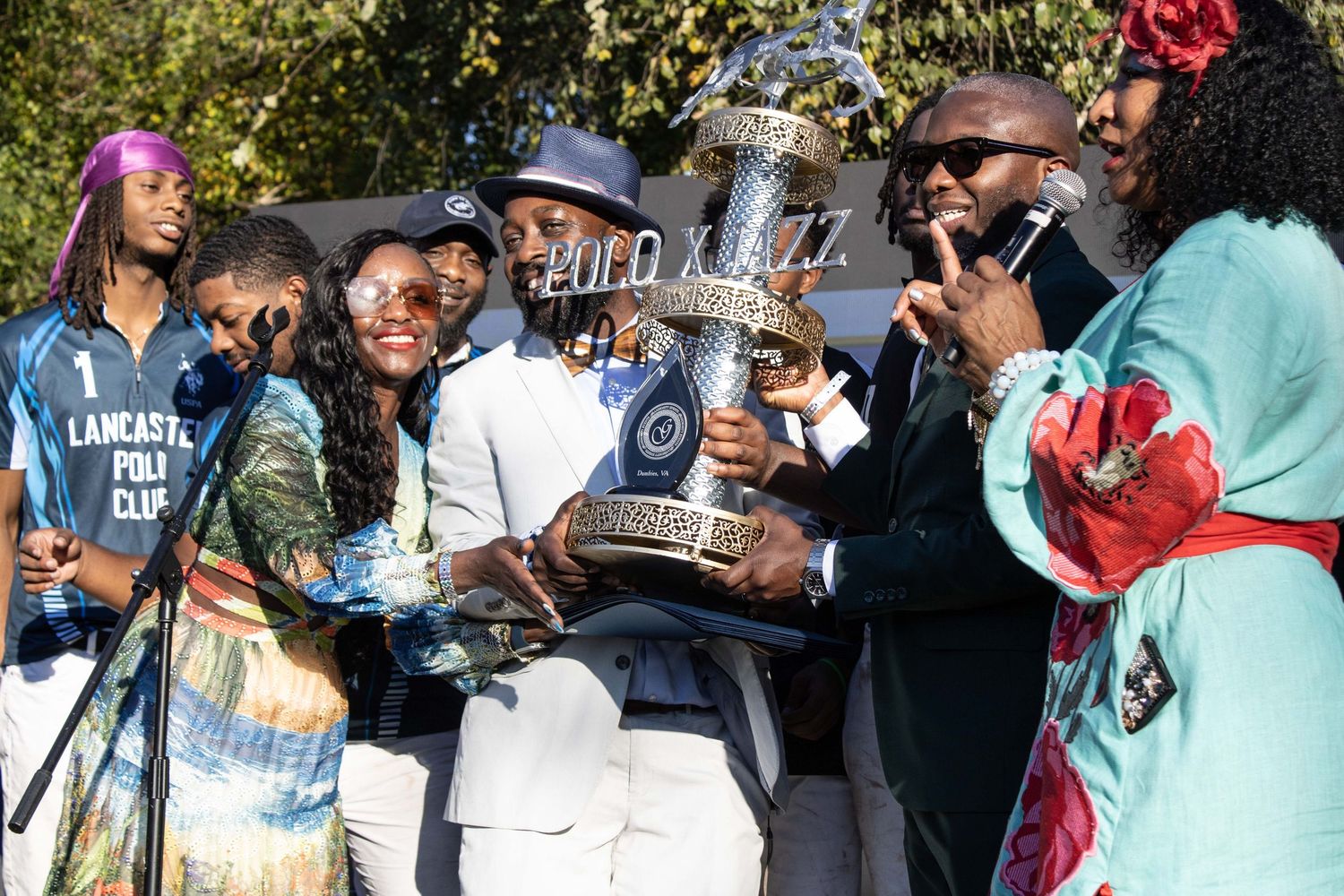 A group celebrates outdoors while holding a large trophy during a festive gathering.