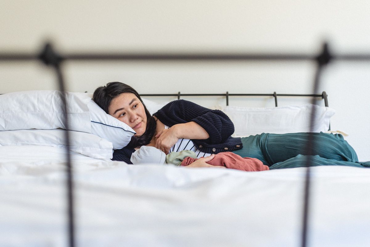 Mother relaxing on bed with newborn during in-home newborn photo session.