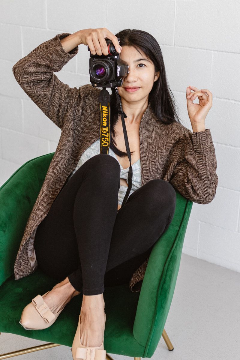 Photographer in brown cardigan sits casually in green velvet accent chair.