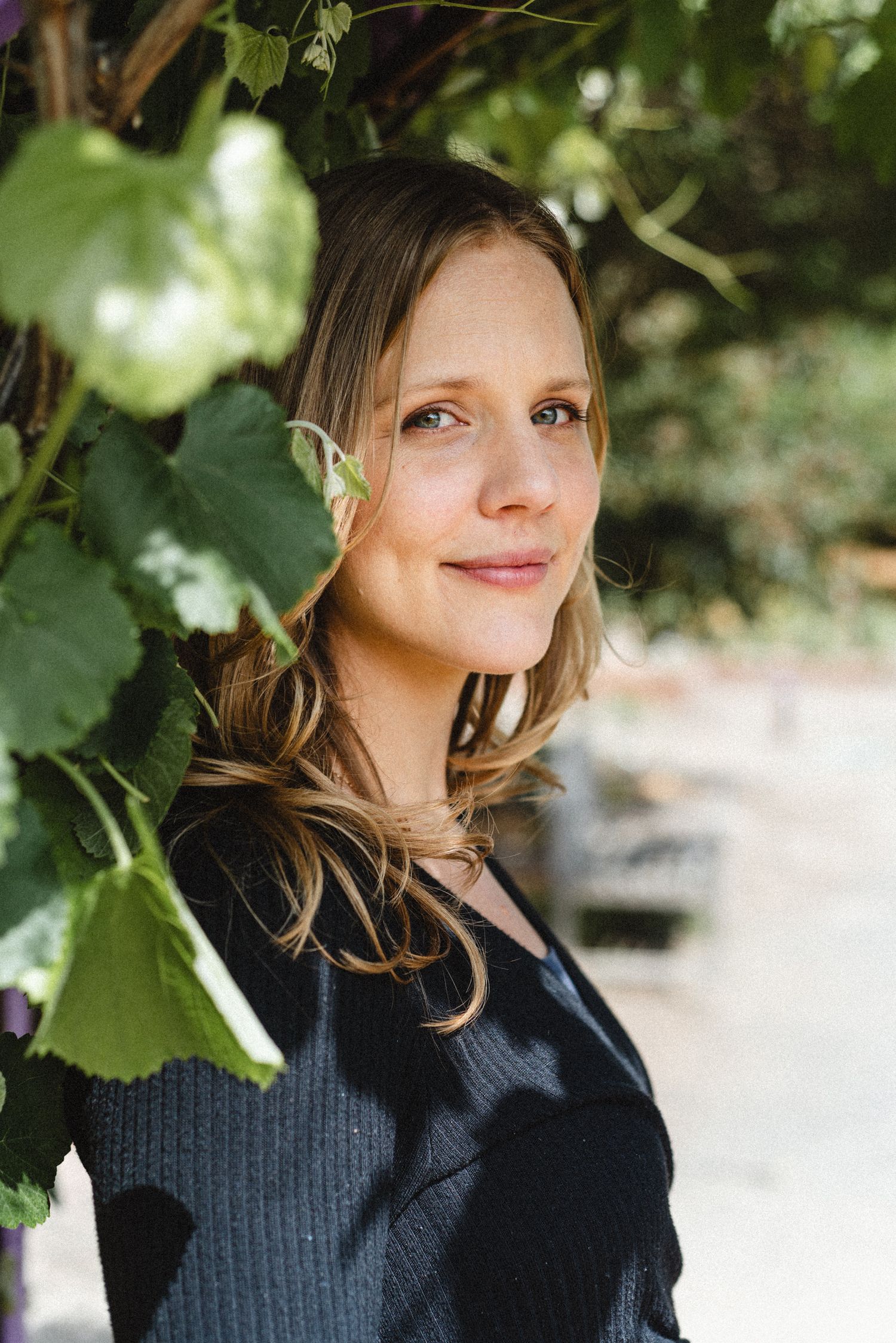 Portrait shot with soft natural lighting showing person outdoors surrounded by green foliage.