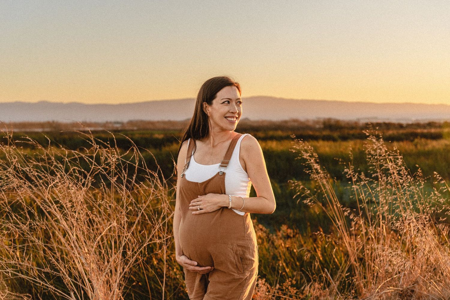 Maternity photo session client glowing in golden field in Fremont, CA with San Mateo glowing across the San Francisco Bay.
