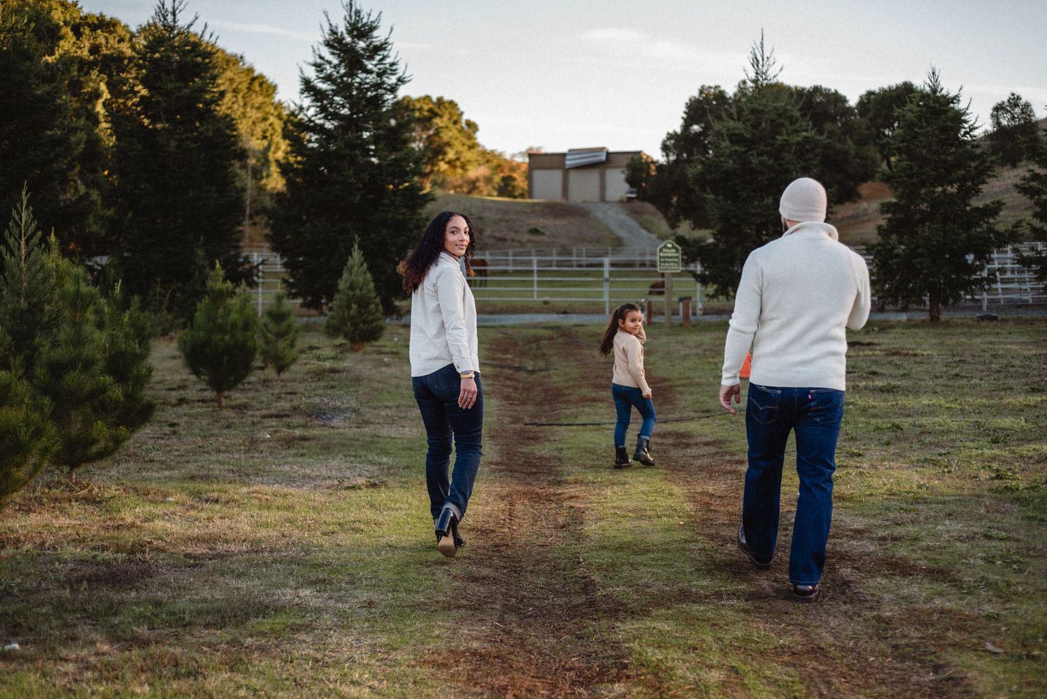 Family taking a relaxing evening stroll on a dirt path surrounded by evergreen trees.