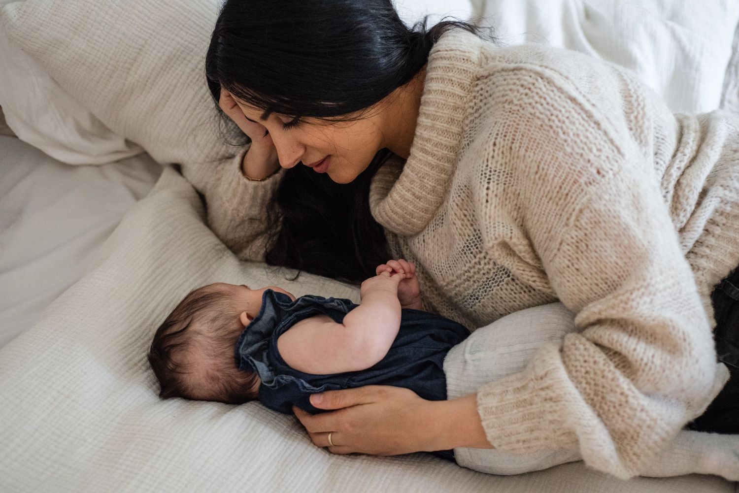 Mother in cozy sweater caring for infant on white bedding.