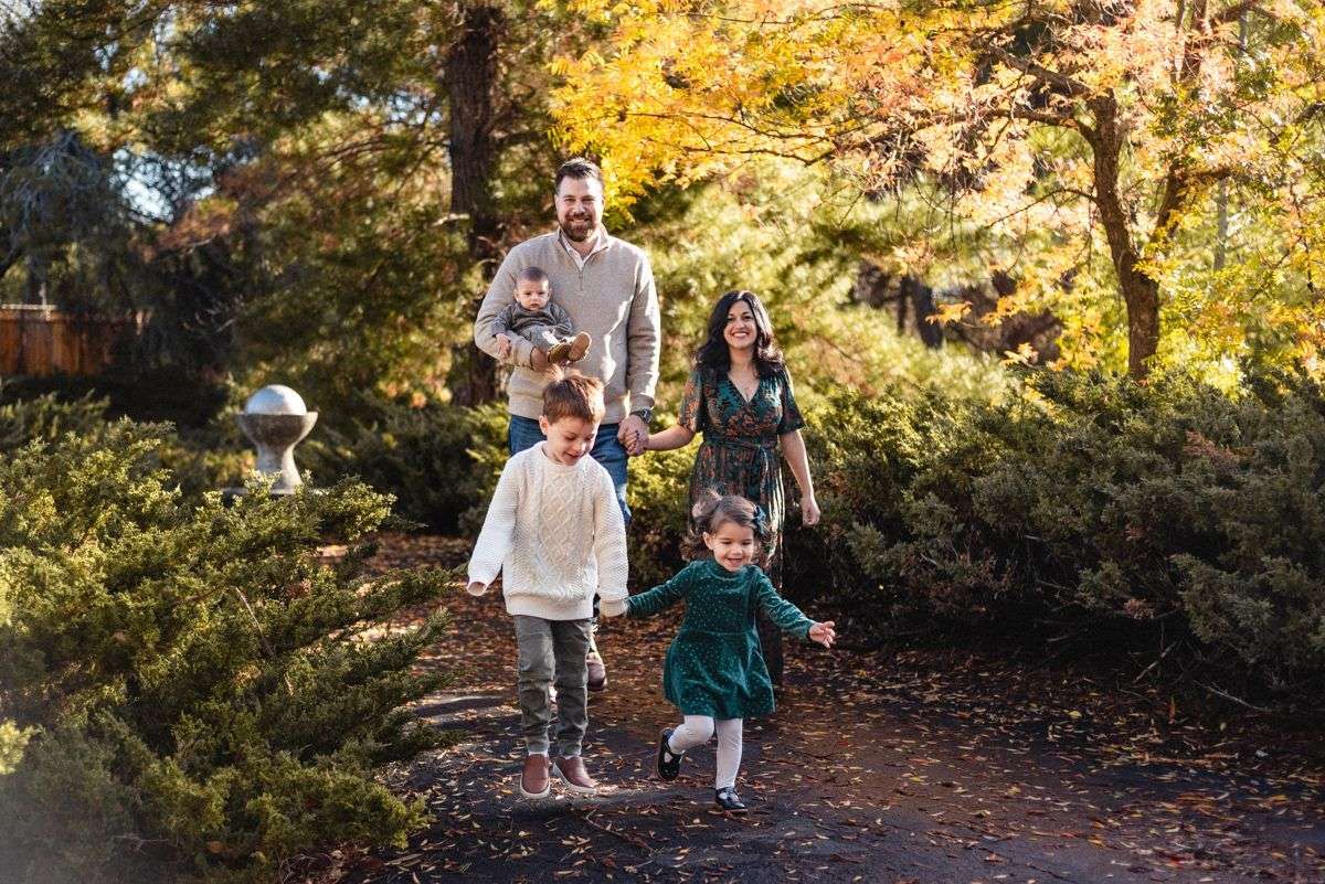 A family walks together on a leaf-covered forest trail during a bright autumn afternoon.