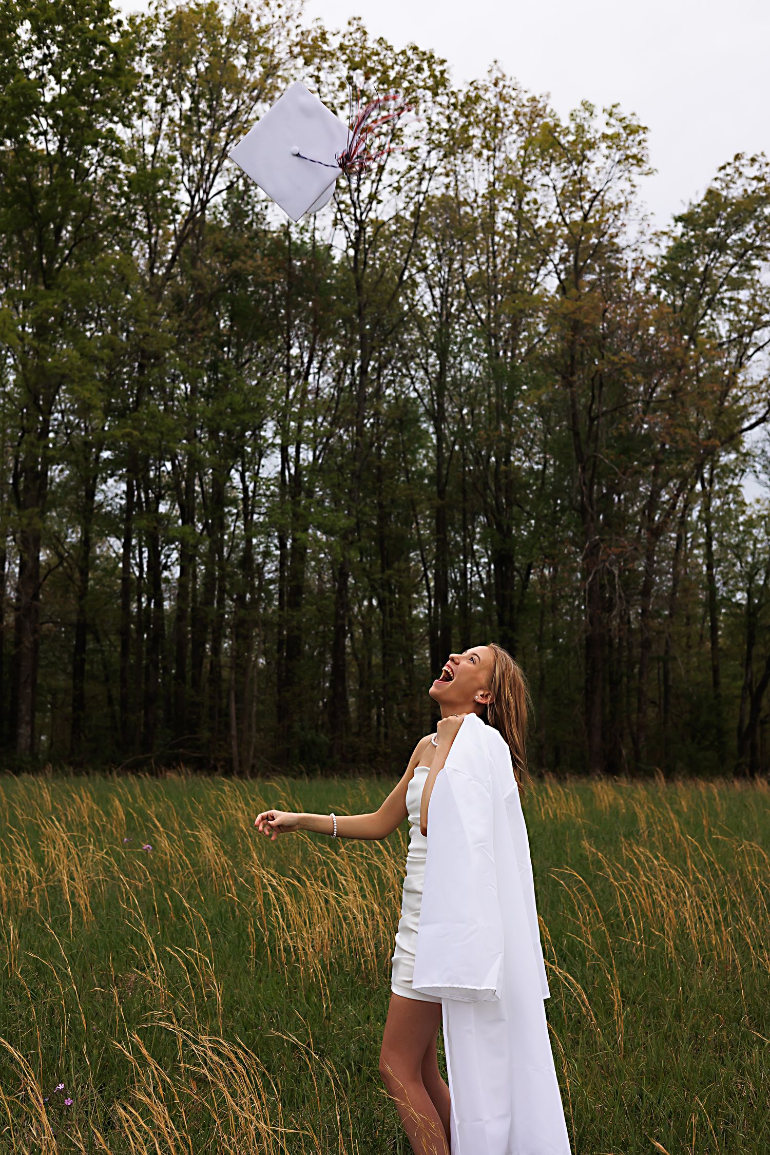 A person in a white dress stands in a grassy field surrounded by tall trees during golden hour.