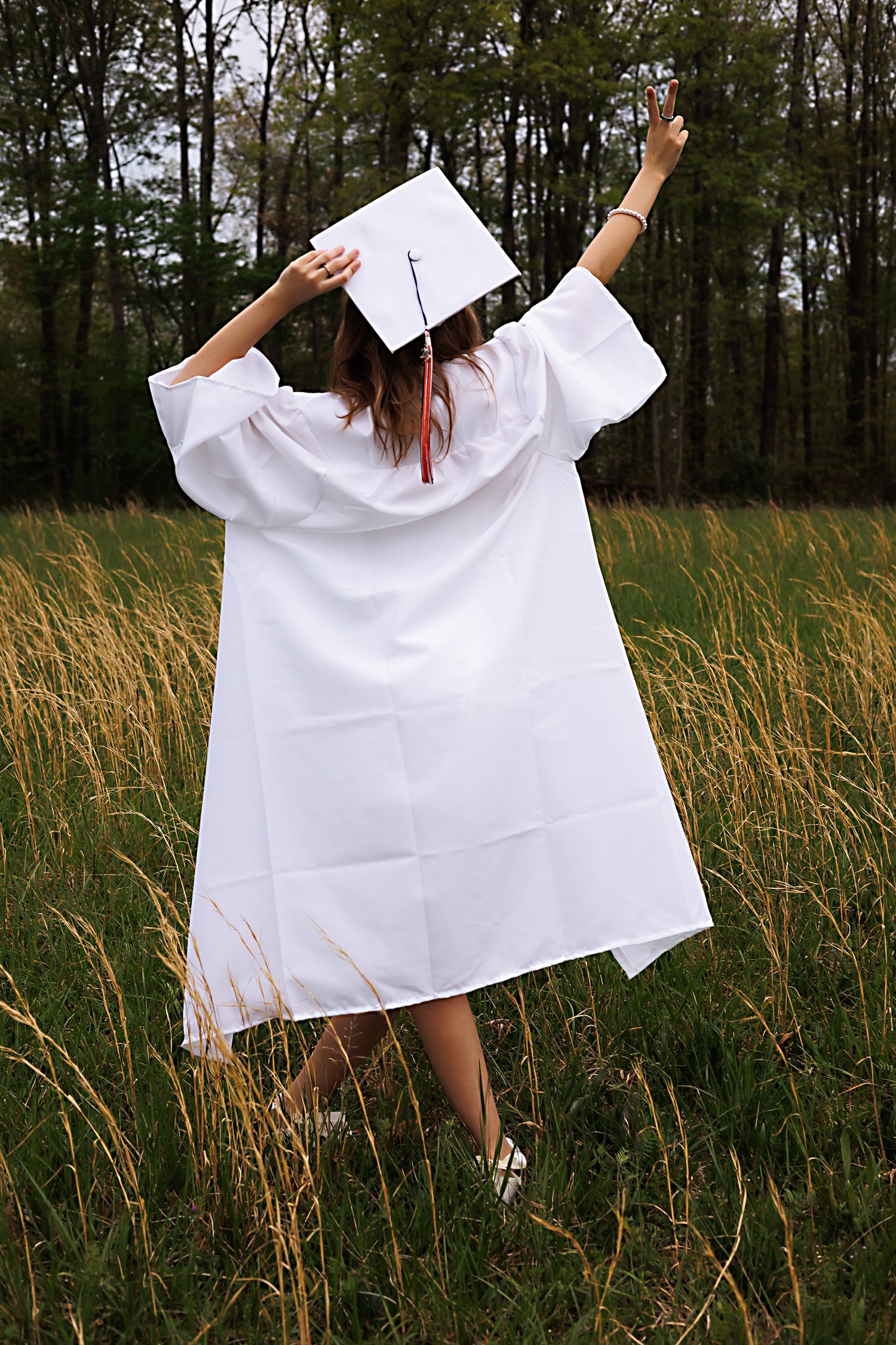 A person in a flowing white dress dances gracefully through tall grass in a field near the forest.