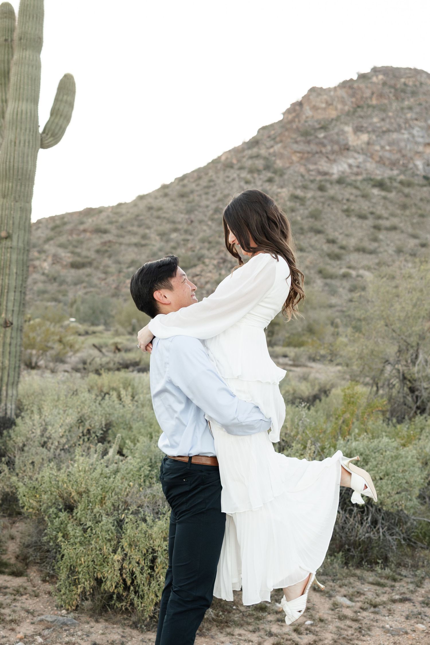 A romantic desert photoshoot with towering saguaro cacti and mountains in the background.