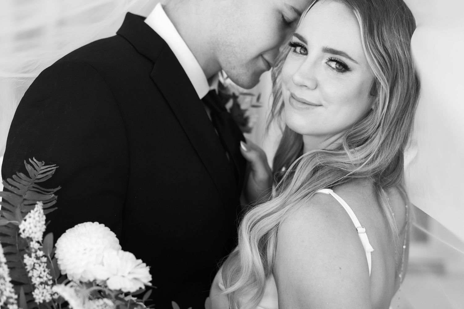 A black and white wedding photo shows a tender moment between a couple with a bouquet.