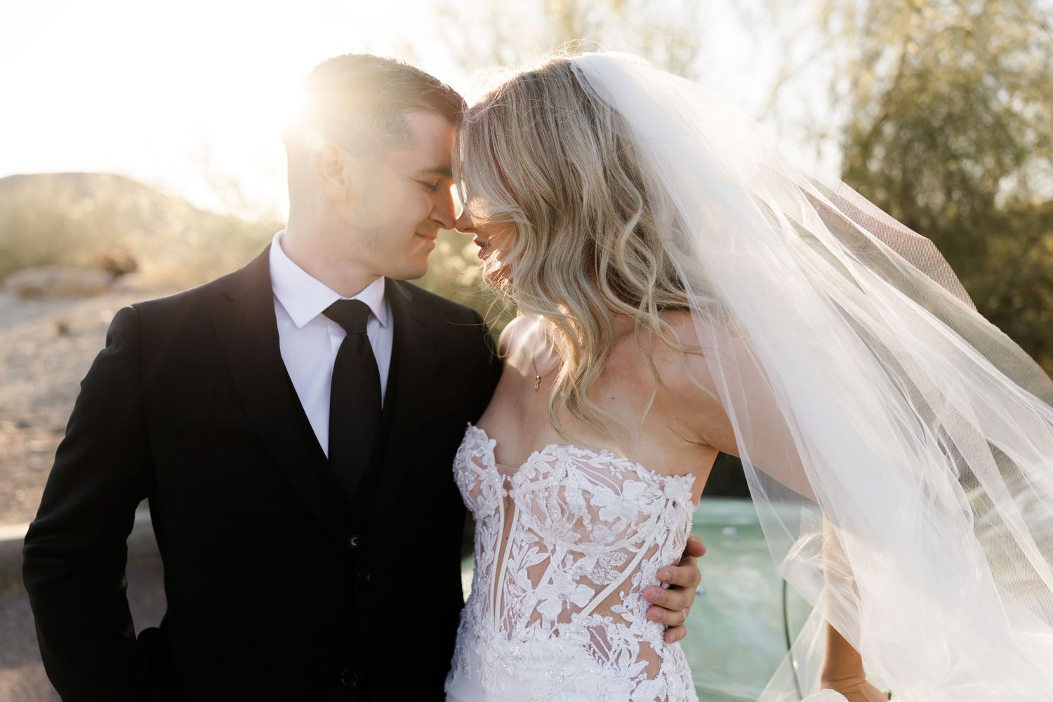 A bride and groom share an intimate moment outdoors, with golden sunlight glowing behind them on their wedding day.