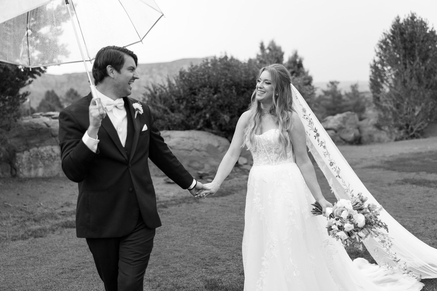 A black and white photo of newlyweds walking hand in hand outdoors.