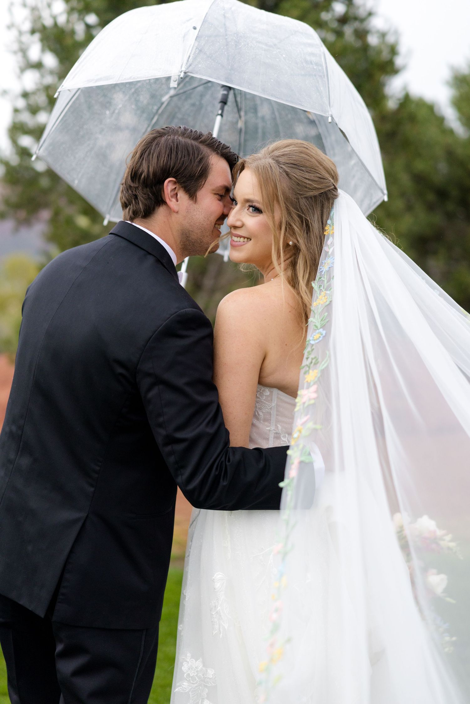 A romantic wedding moment shared under a clear umbrella in the rain.