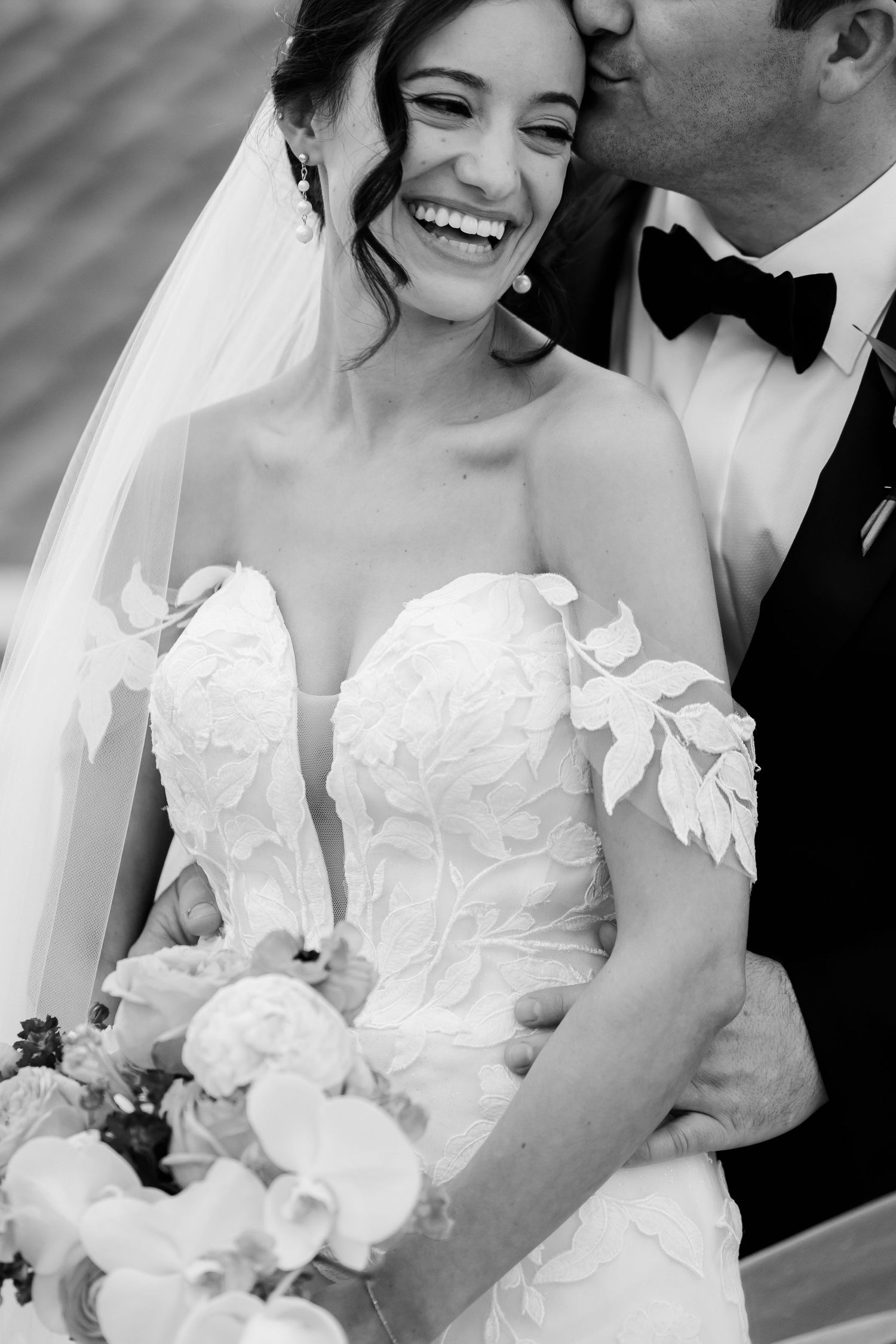 A joyful moment captured in black and white as a bride in a strapless wedding gown laughs while holding her bouquet.