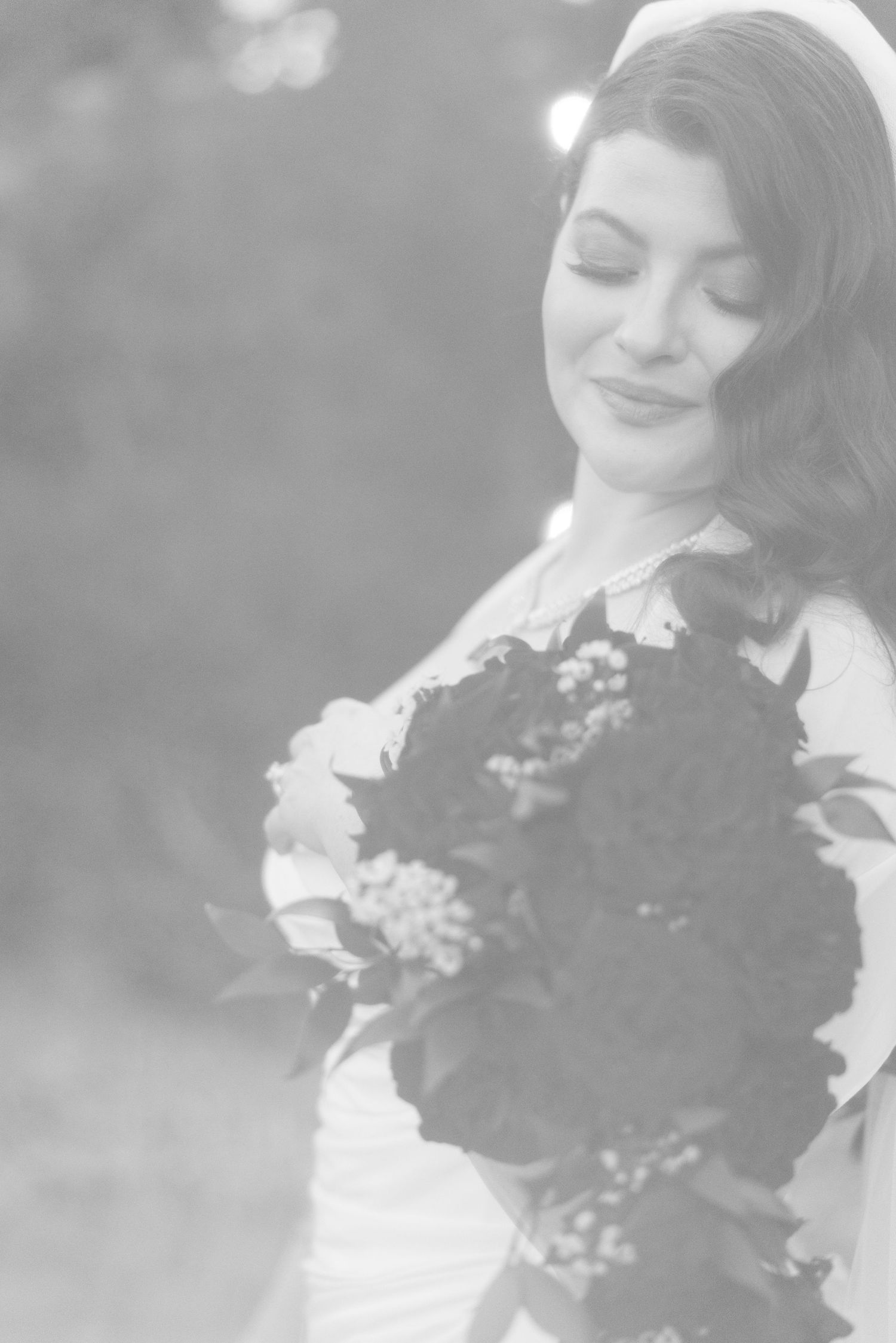 Black and white wedding portrait of a person in a white dress holding a bouquet with eyes closed and a gentle smile.