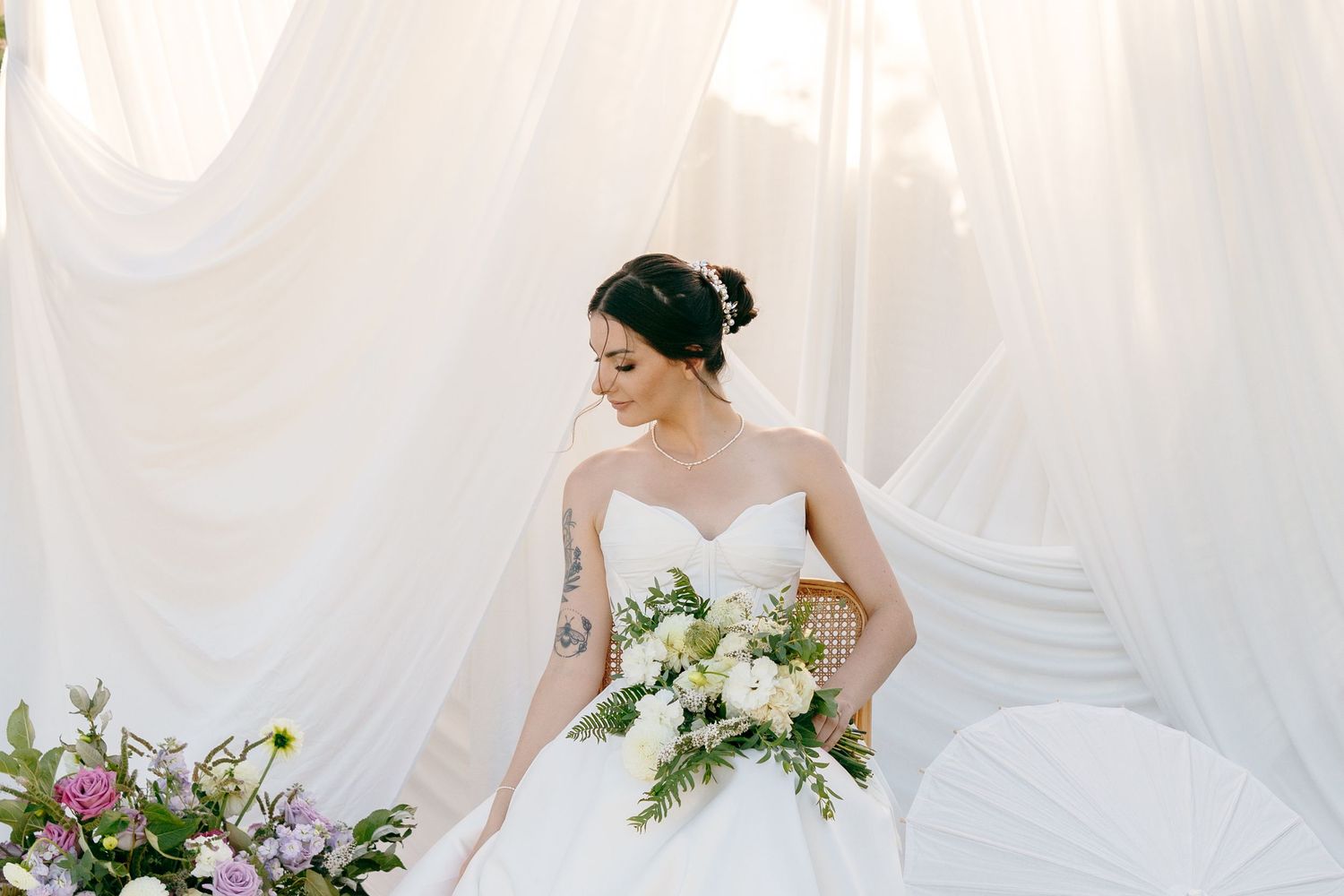 A bride in a white wedding dress holds a lush bouquet of white and green flowers against a light background.