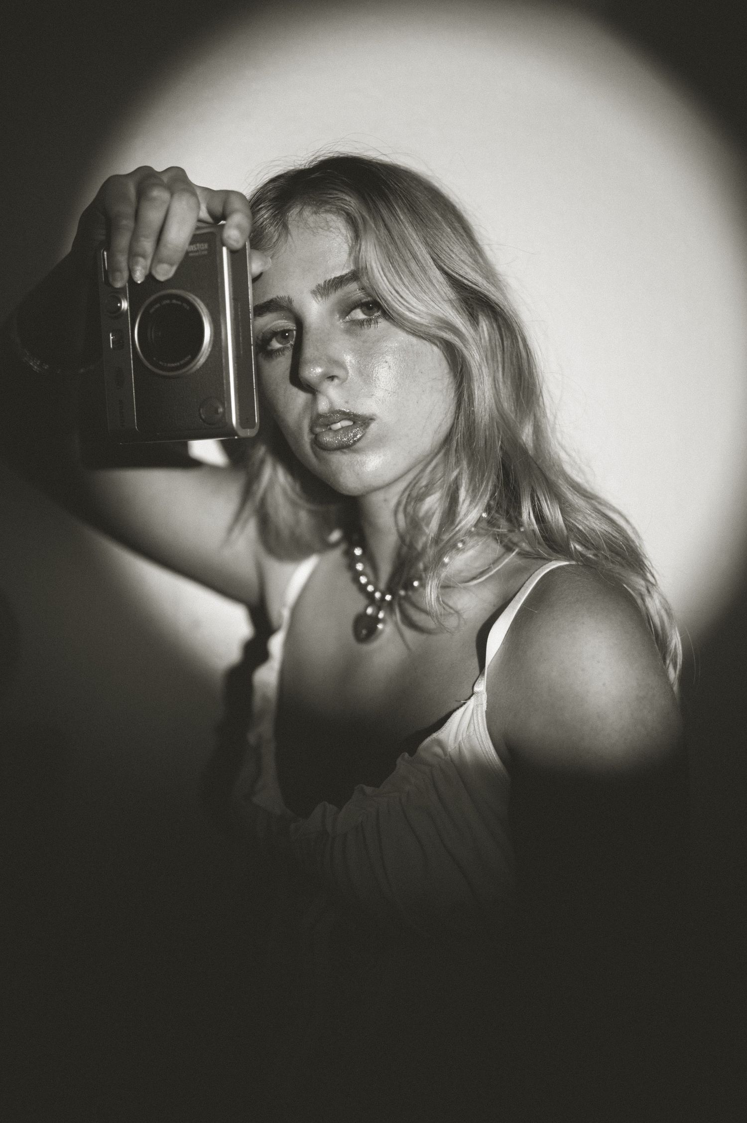 Young blonde woman holding a vintage camera up in a moody black and white portrait photo.