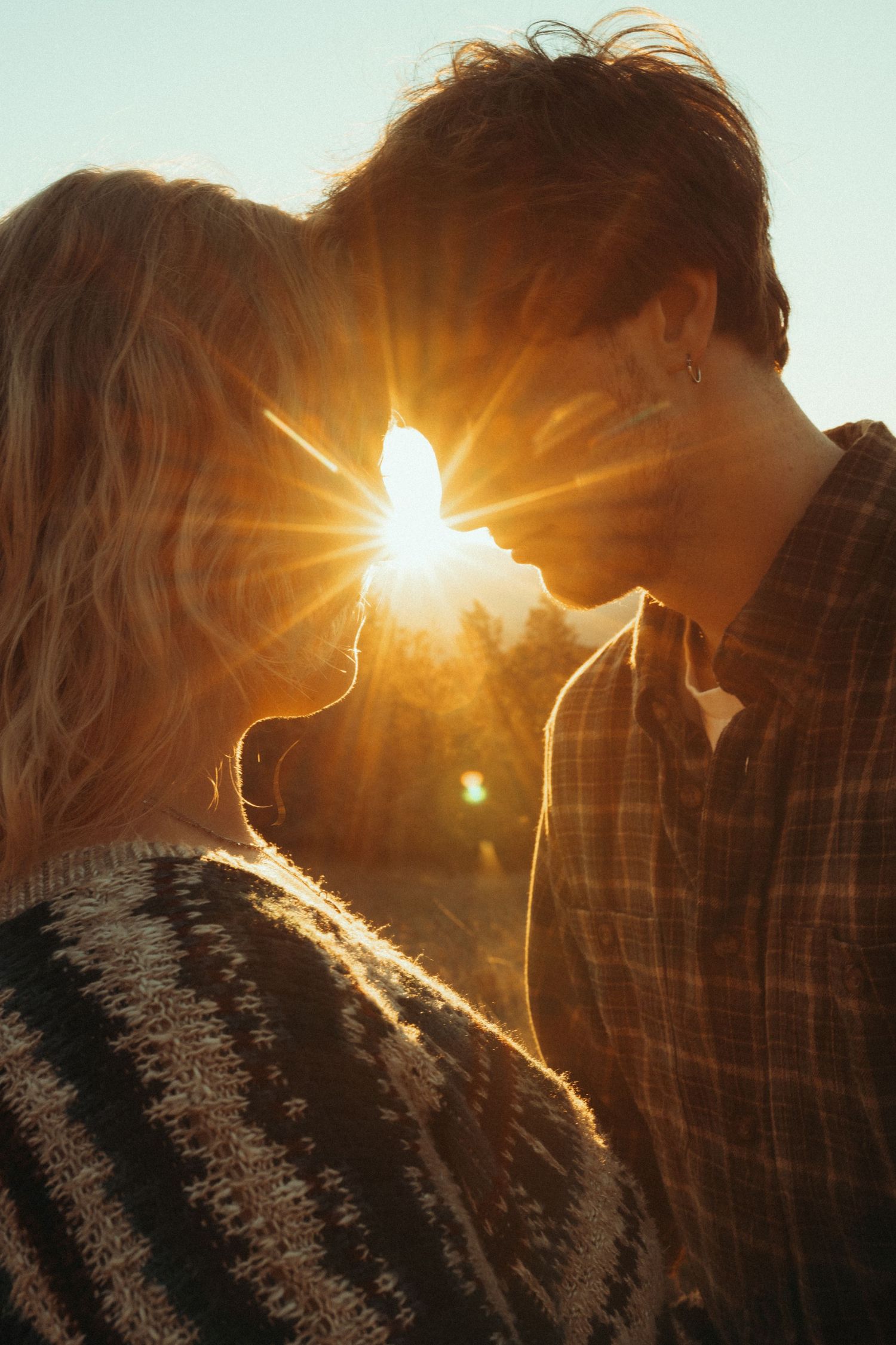 Sunlight bursts through mountain peaks creating dramatic lens flares and silhouettes against a golden sky at sunset.