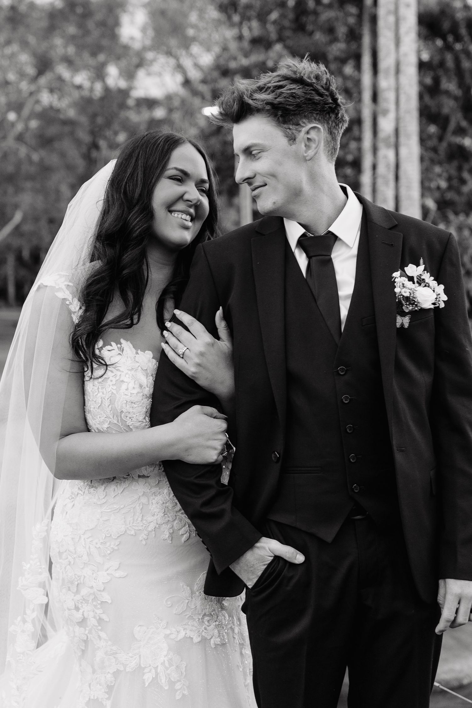 Black and white wedding portrait of a bride and groom sharing a candid laughing moment together outdoors.