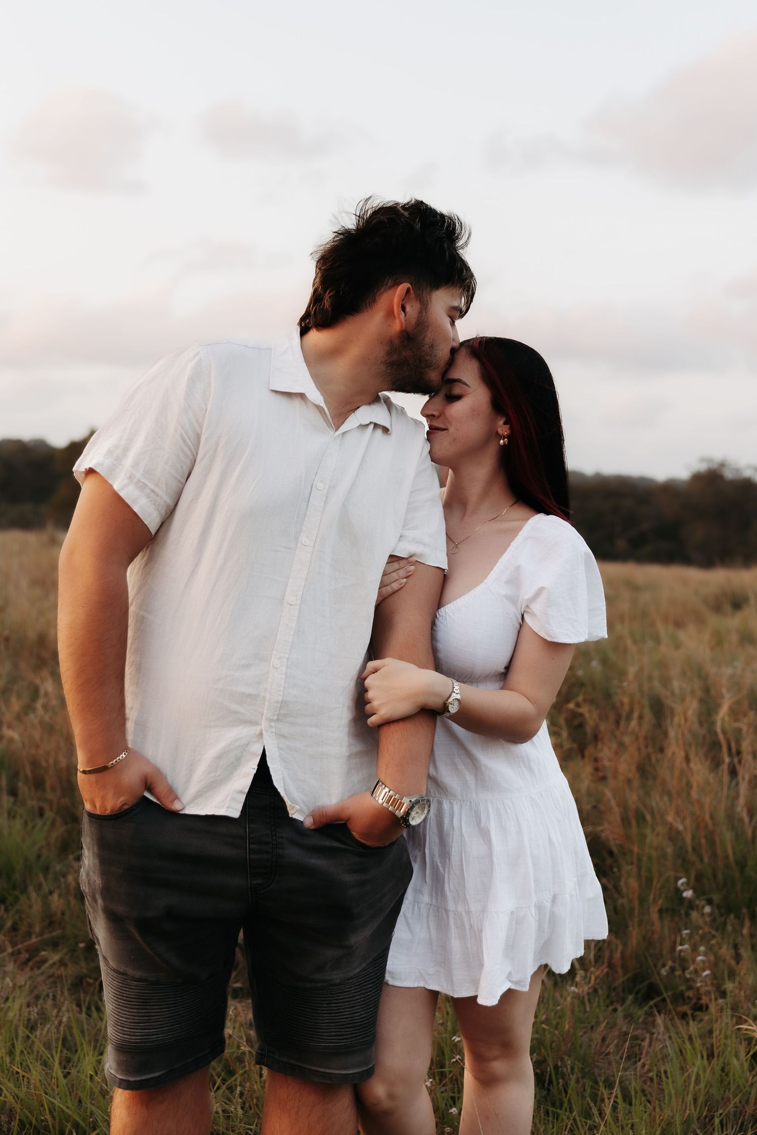 A couple in white outfits share an intimate moment together in a sunset lit field.