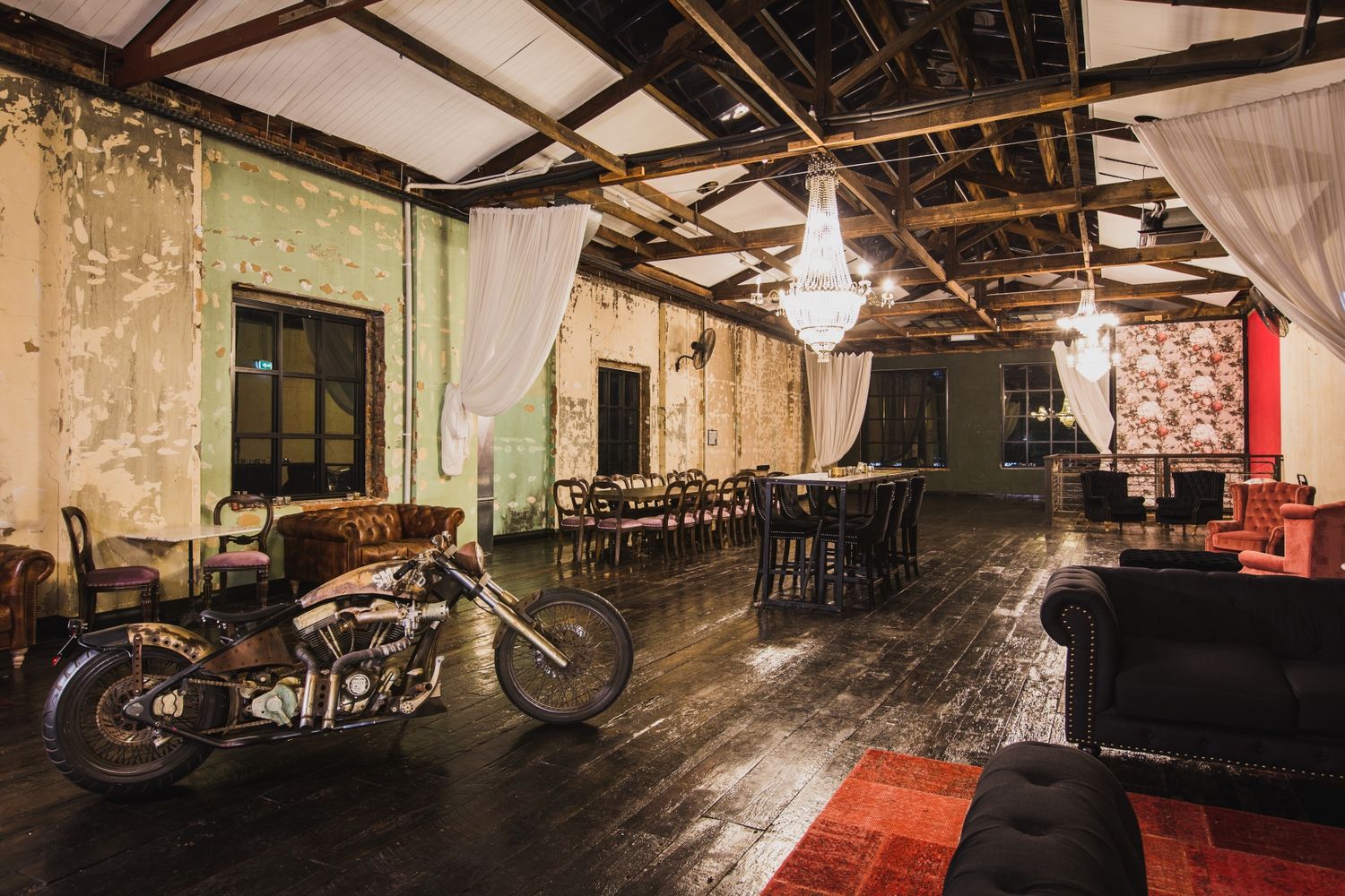 Vintage motorcycle parked inside a rustic industrial venue space with exposed beams and hardwood floors.