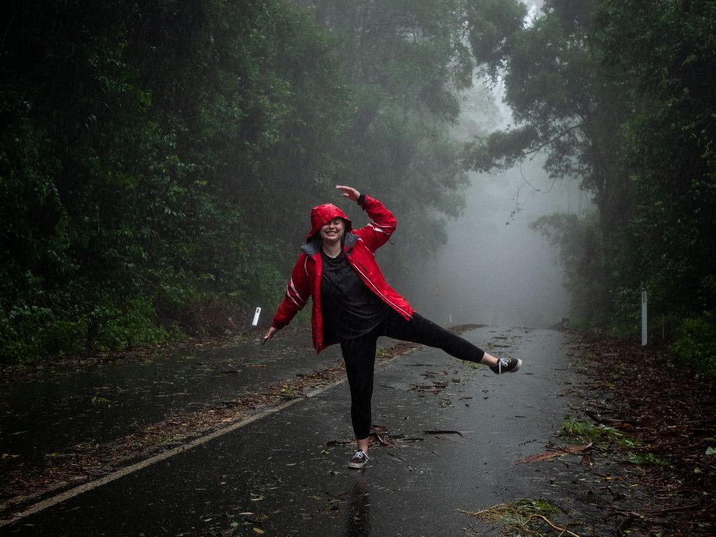 A figure in a bright red raincoat dances playfully on a misty forest path during a foggy day.