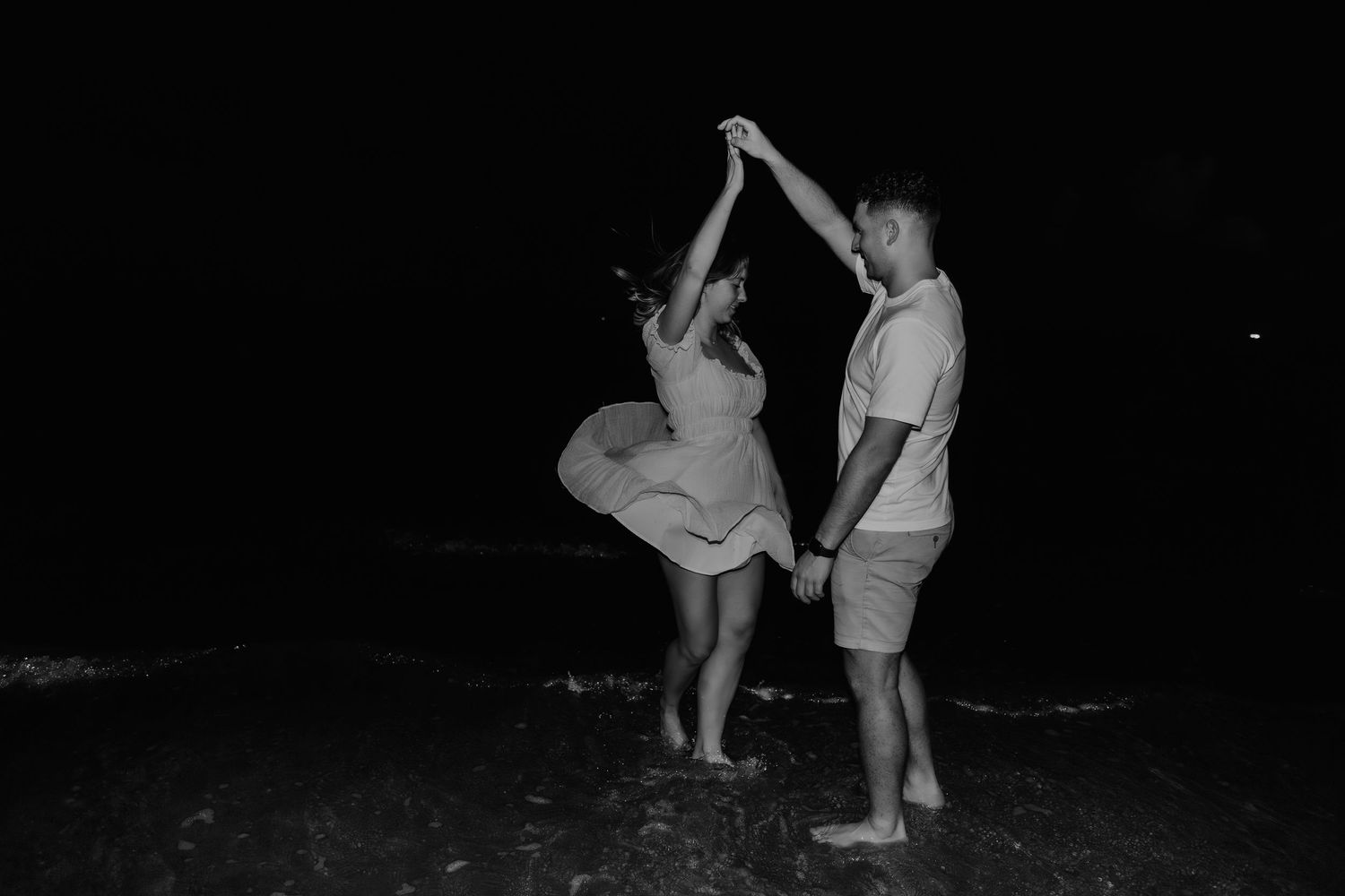 A couple dancing together on a dark beach at night, captured in black and white photography.