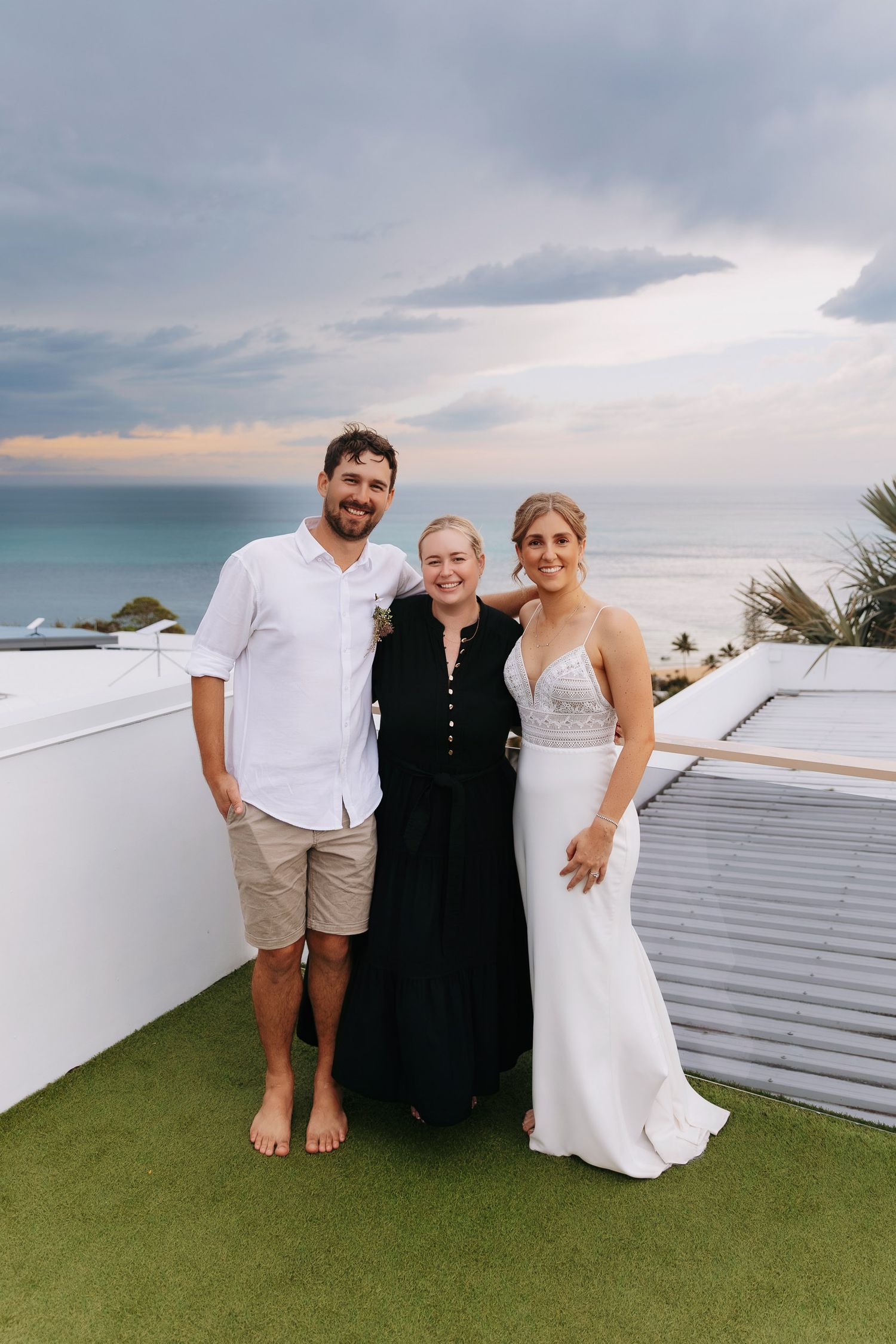 A wedding celebration on a rooftop with cloudy skies and ocean views in the background.