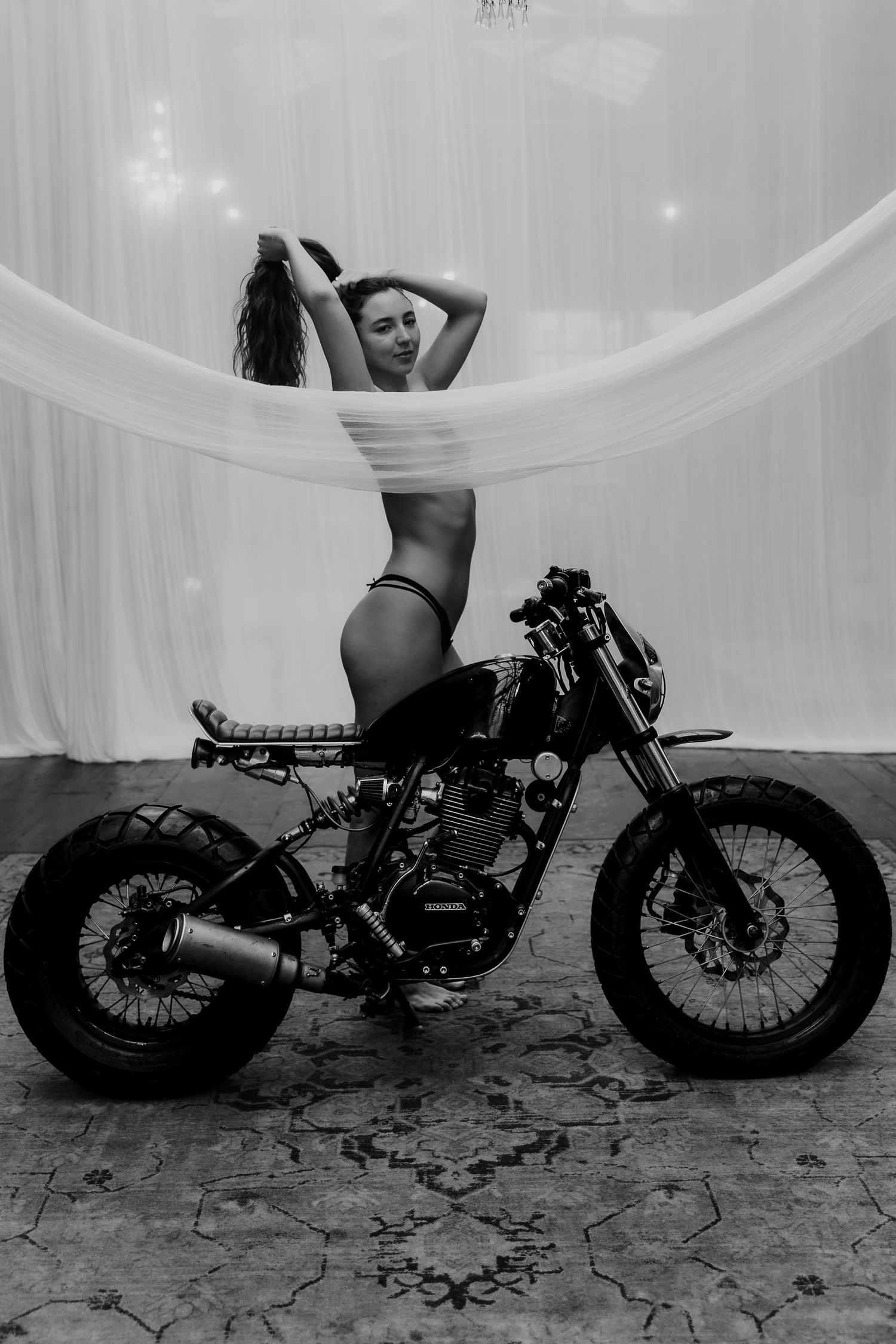 Artistic black and white photograph of a custom motorcycle with flowing white fabric and dramatic artistic pose.