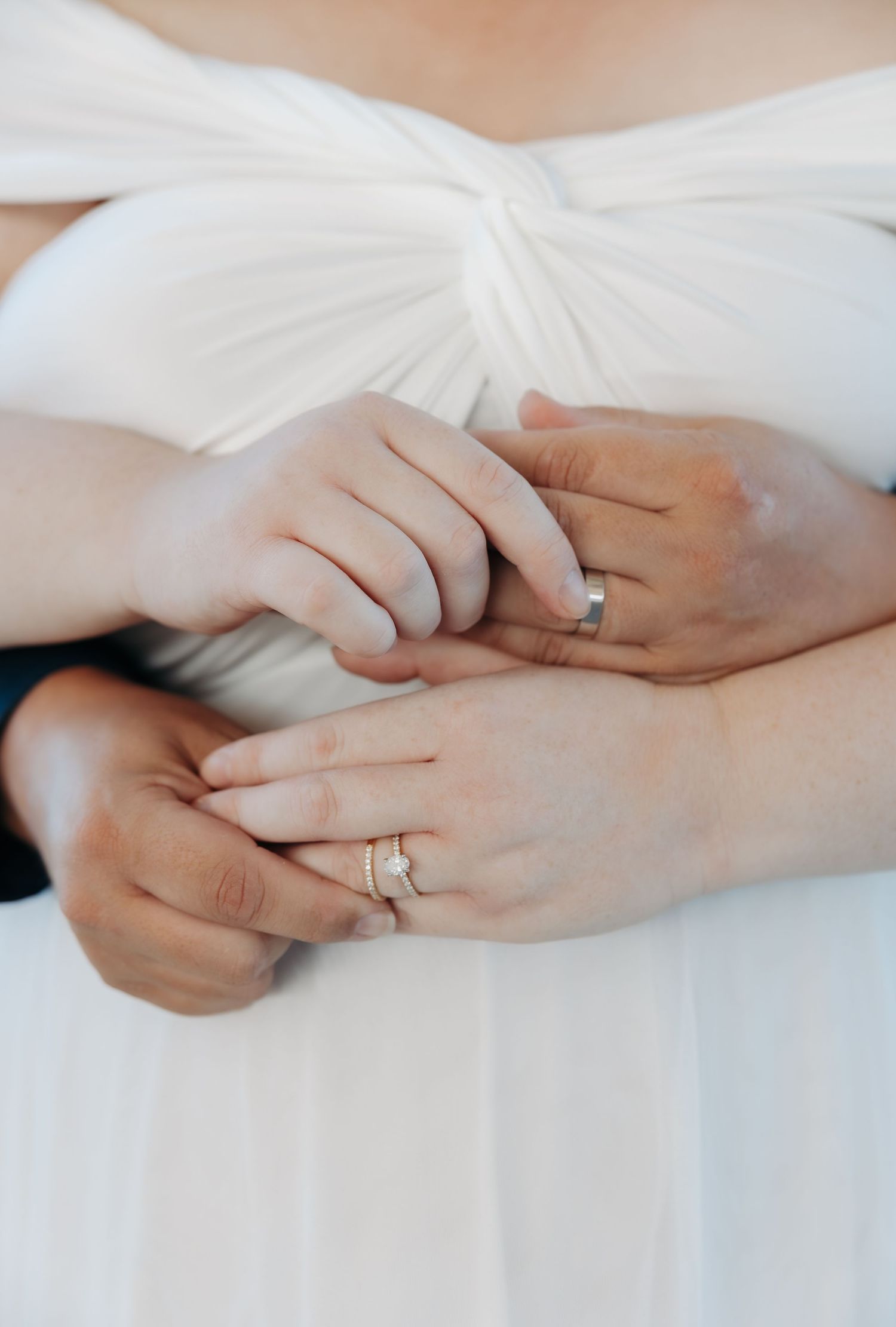Closeup of hands wearing wedding rings against a white dress fabric background.