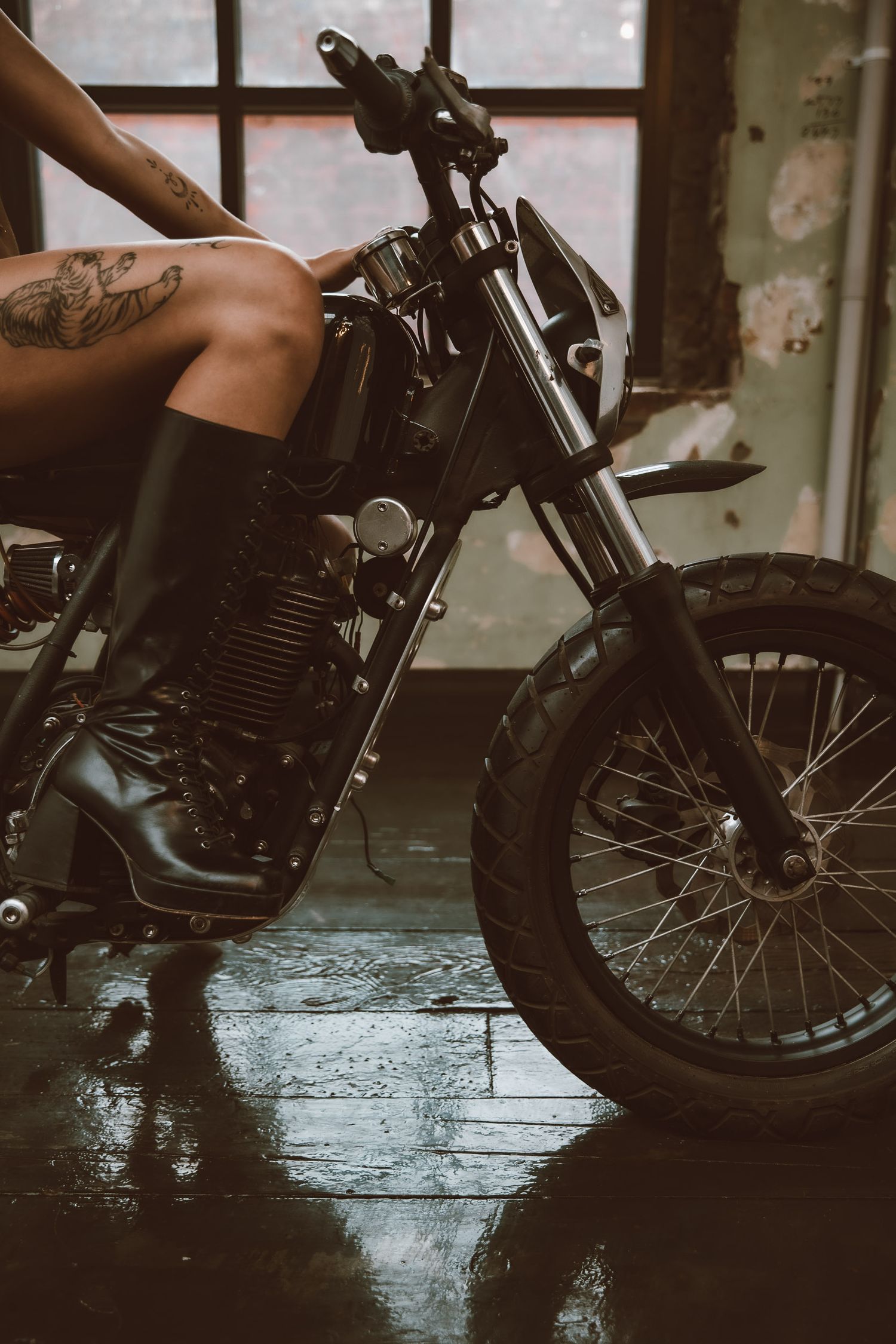 Close-up view of a vintage motorcycle with chunky tires on a wet floor showing handlebar details and partial frame.