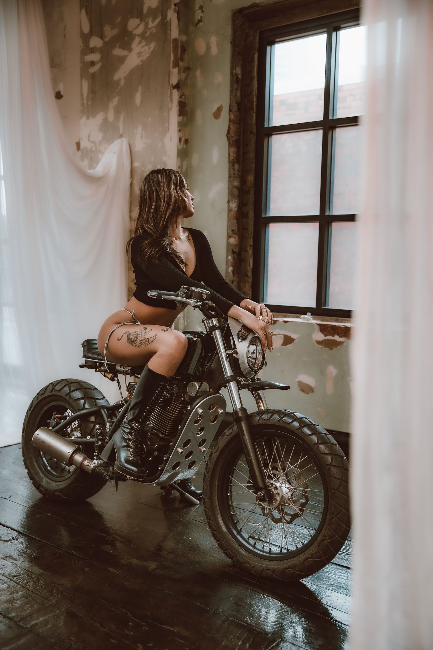 A vintage motorcycle is parked indoors by a window, with soft natural light creating a moody atmosphere.