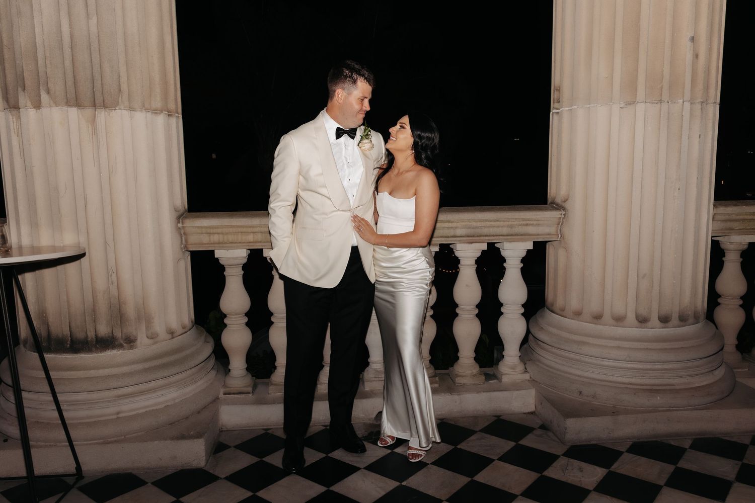 A romantic wedding photo shoot captured at night with couples posing between illuminated white stone columns.