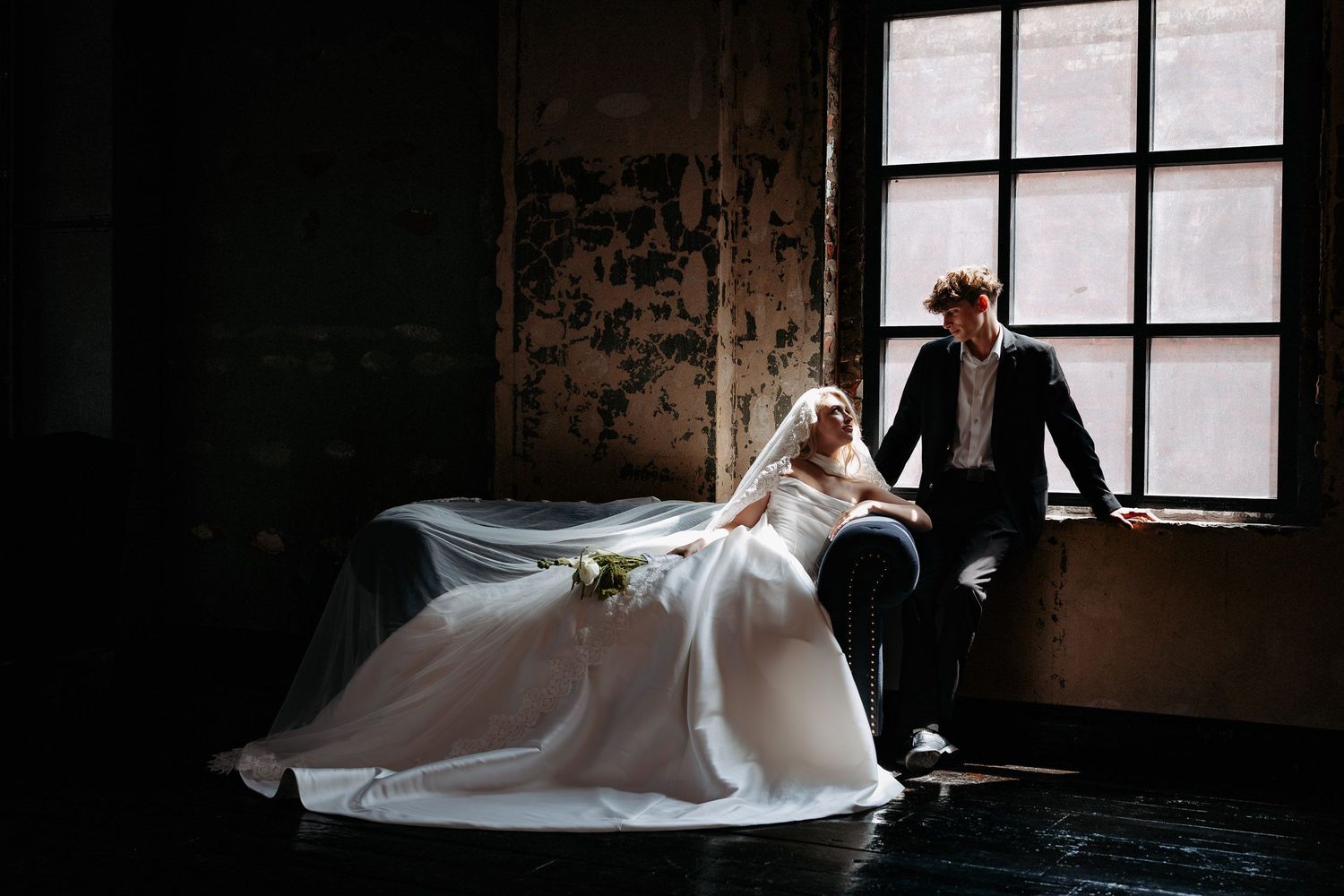 A series of moody bridal portraits in a rustic setting with dramatic window lighting and flowing white gowns.