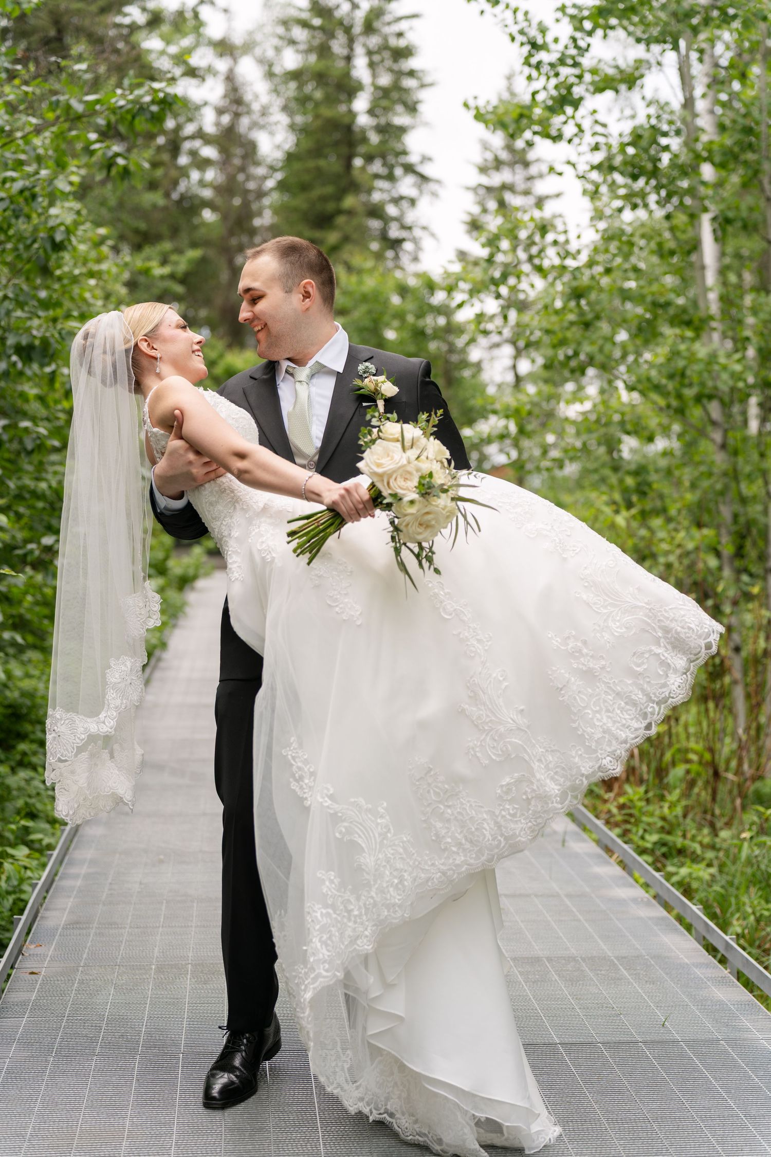 Romantic couple in wedding attire share an intimate dip dance pose on a patio surrounded by lush greenery.