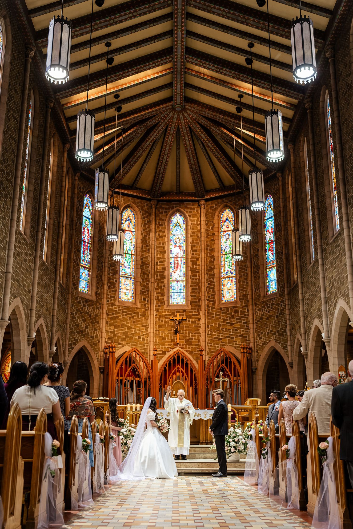 Bride and groom exchange vows at a stunning church altar with stained glass windows and vaulted wooden ceiling.