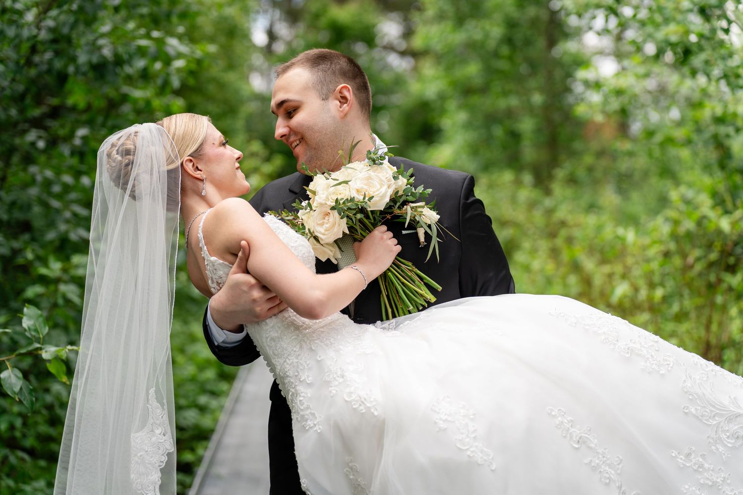 A romantic wedding couple embraces in a lush garden setting with greenery and flowers in the background.