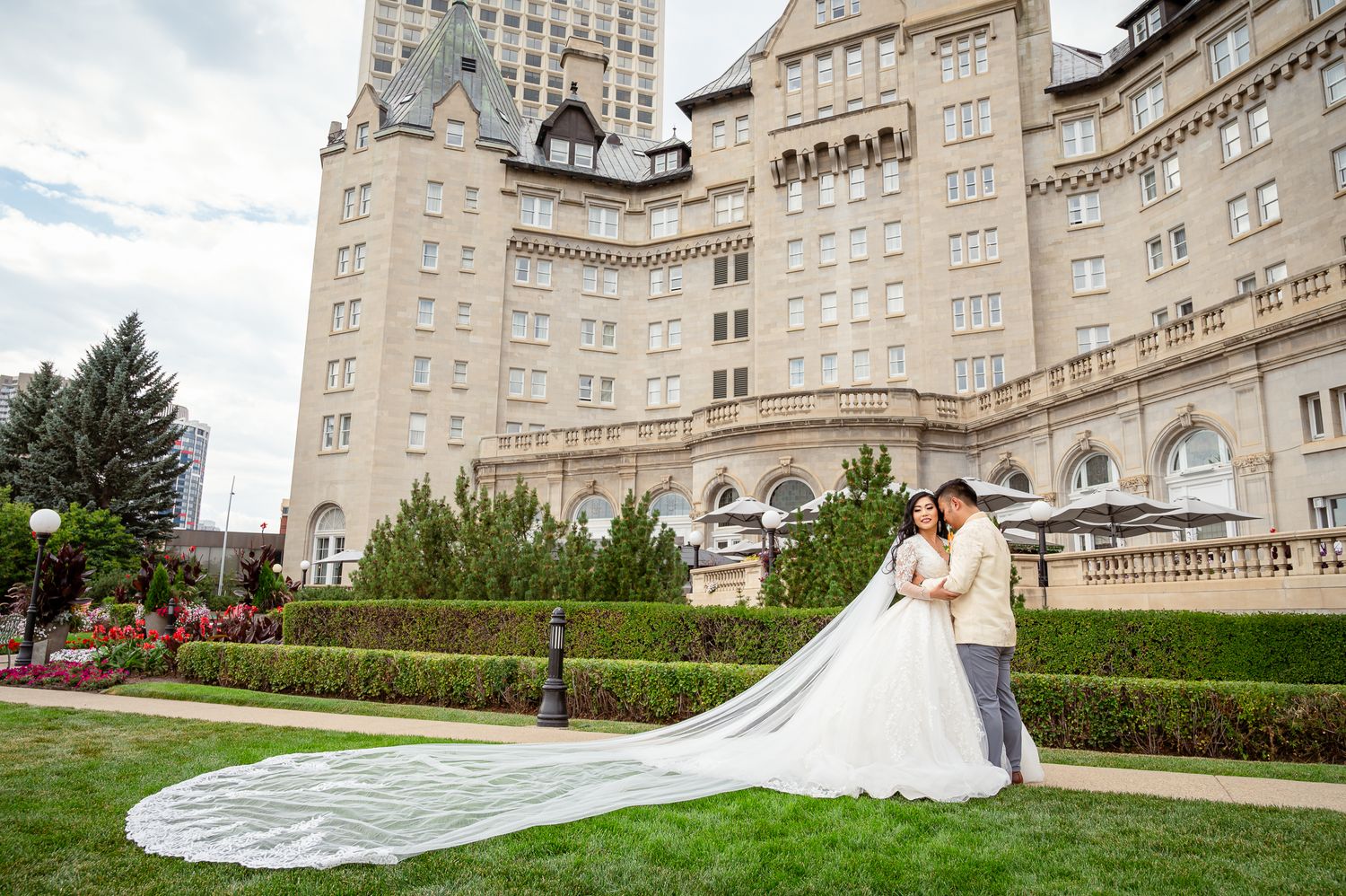 Bride and groom pose in front of Fairmont MacDonald hotel with  bride wearing a long cathedral veil.