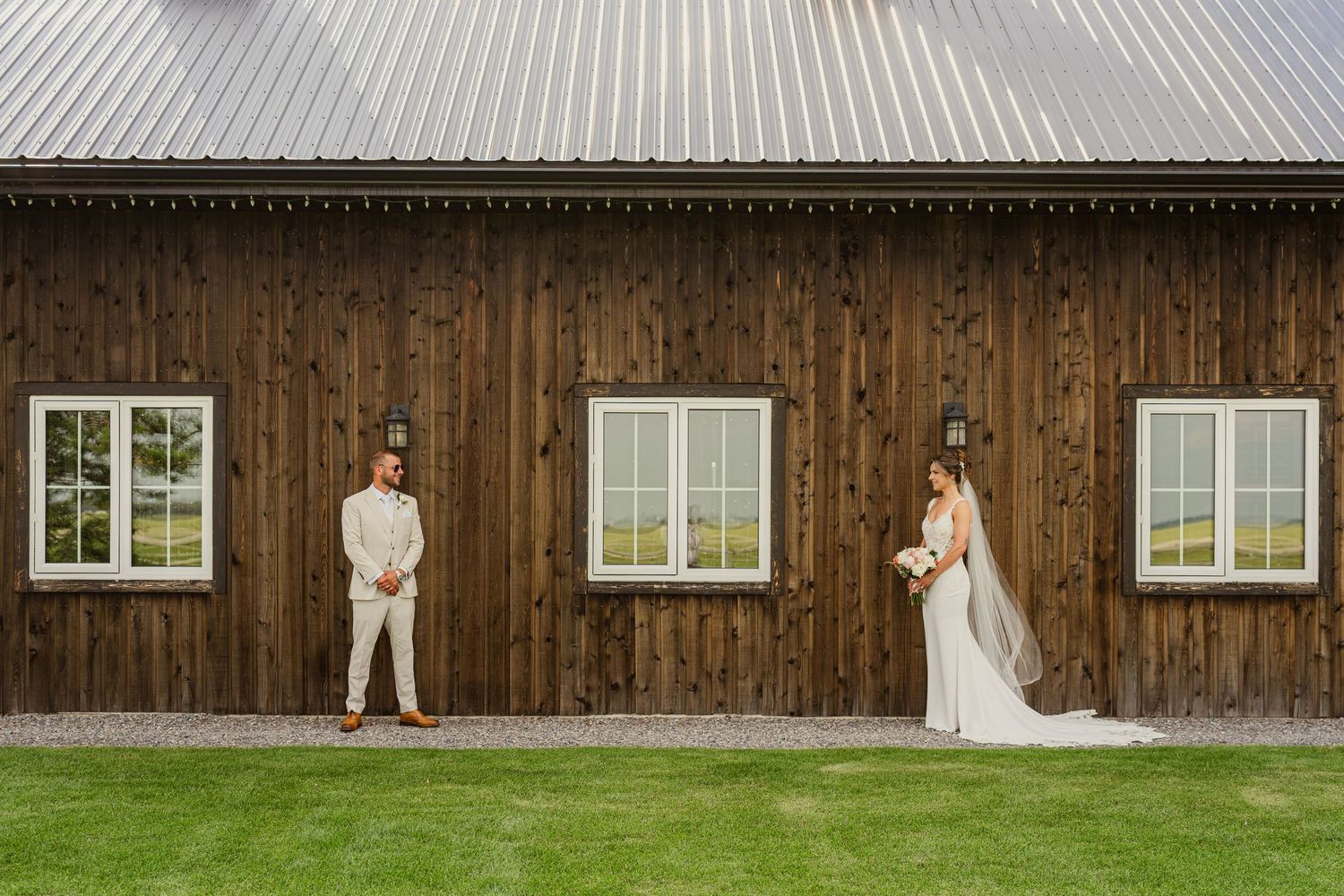 Bride and groom pose apart in front of a rustic wooden barn on their wedding day At Free Spirit Ranch.