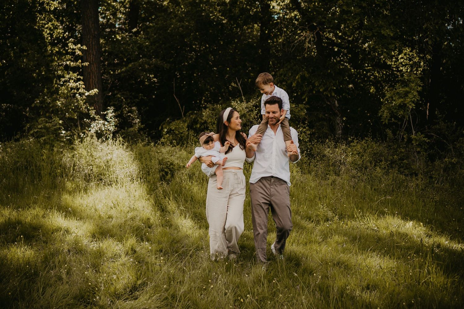 A family walking together through a sun-dappled meadow on a warm summer day.