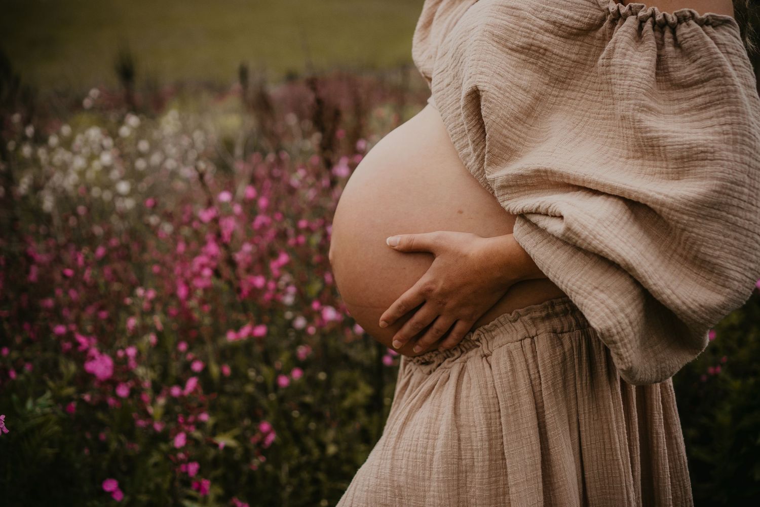 A series of photos showing a maternity shoot in a beige dress with pink wildflowers in the background.