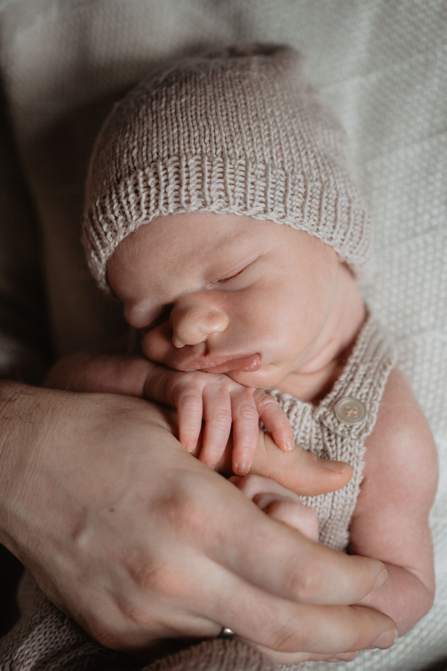 Peaceful sleeping newborn baby wearing knitted beanie hat while being cradled by gentle hands.