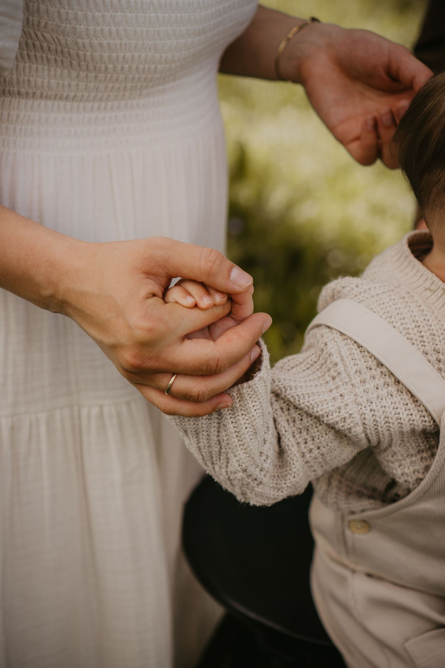 Close-up of hands holding, showing a white dress and knitted sleeve, suggesting an intimate family moment.