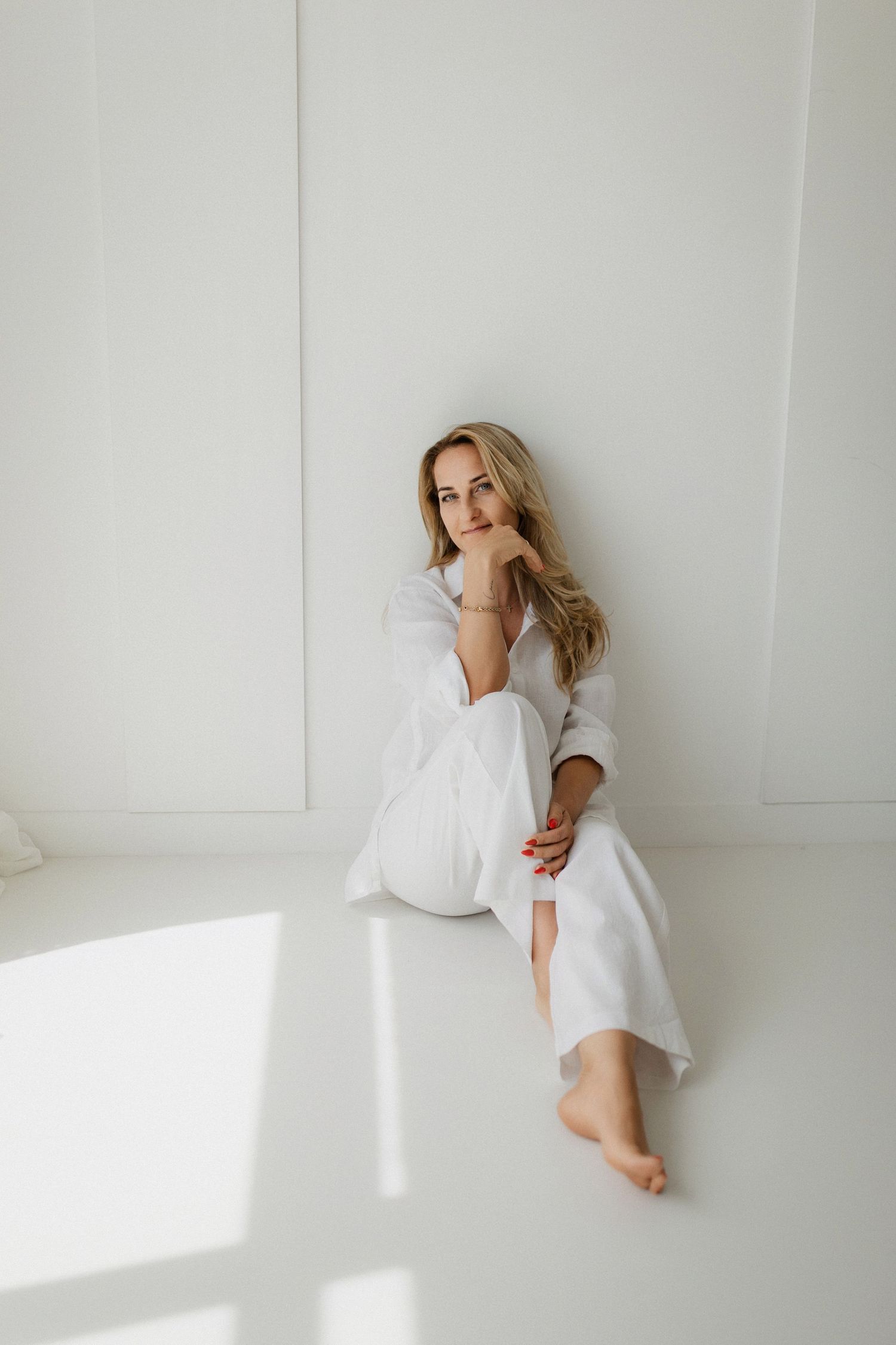 Minimalist artistic photo series of someone in white clothing against plain white walls with dramatic natural lighting.