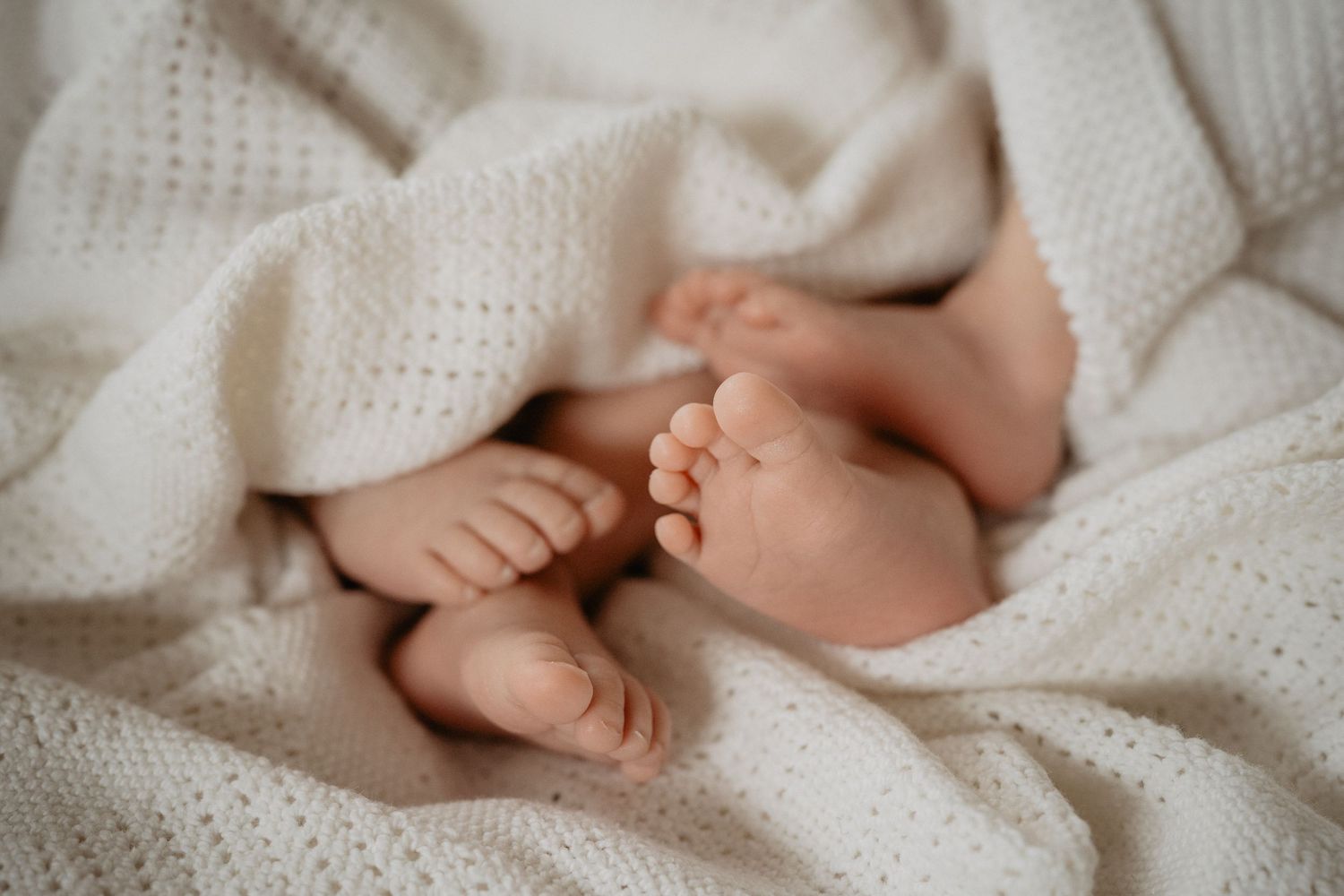 A series of tender close-up photos showing tiny baby feet against soft white knit blankets.