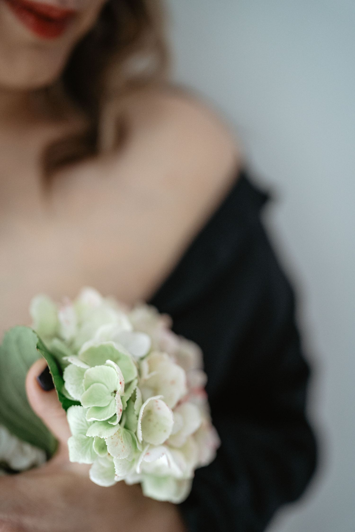 A delicate white hydrangea flower arrangement is held against a black garment in soft muted lighting.