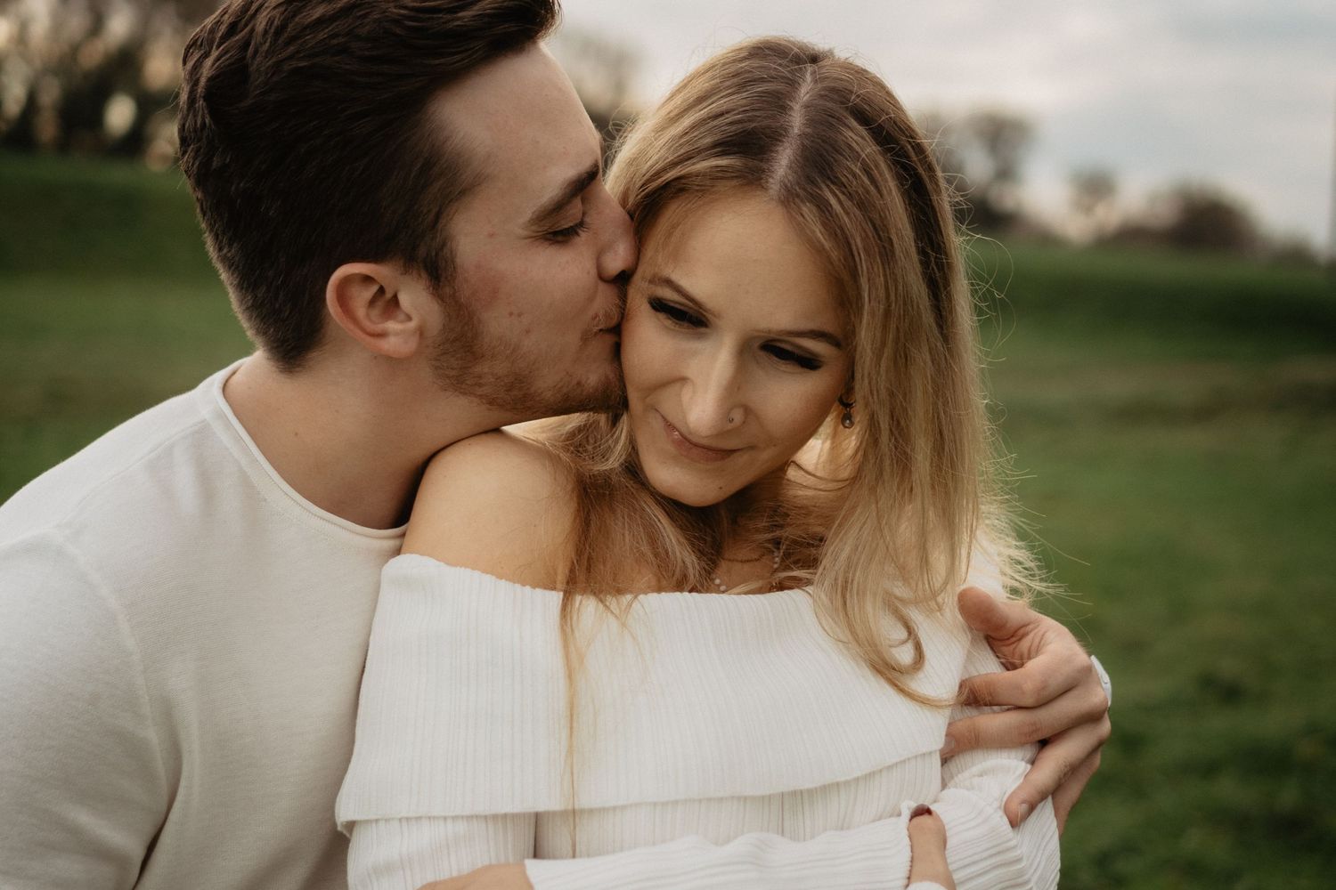 A tender romantic moment between a couple embracing outdoors in a grassy field during golden hour.