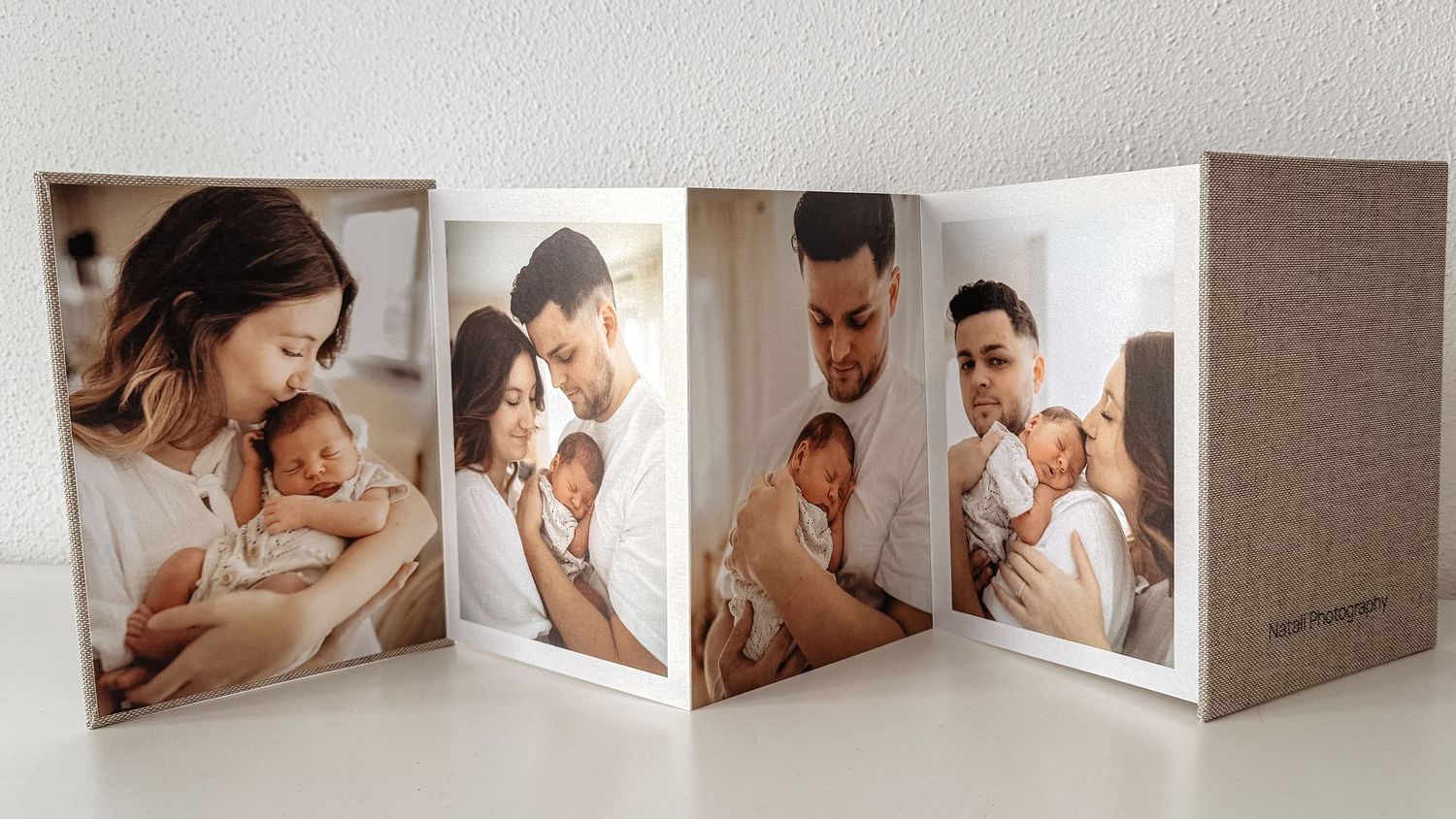 A folded photo album displays candid intimate parenting moments in muted neutral tones on white background.
