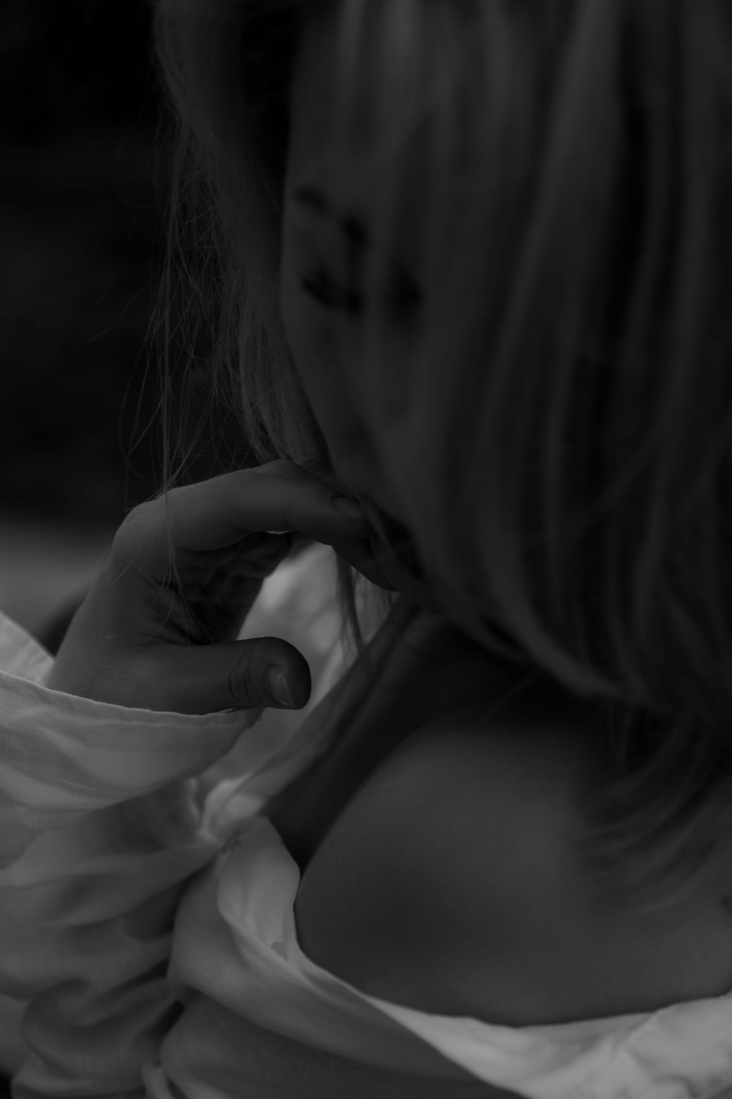 A black and white artistic portrait showing someone resting pensively in soft lighting with flowing hair.